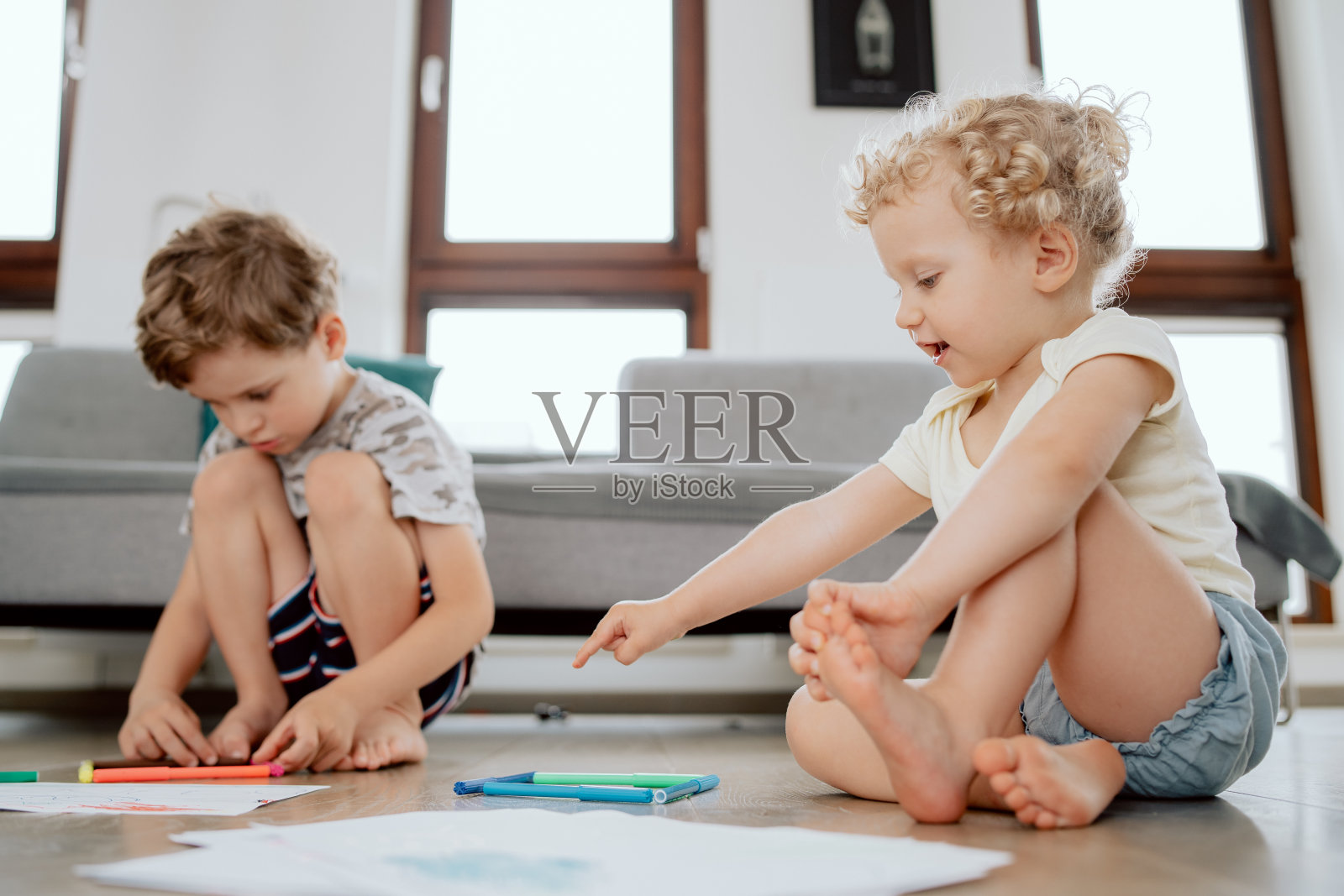 一个学龄期的男孩和一个学龄前的女孩坐在家里客厅的木地板上，用彩色记号笔作画照片摄影图片