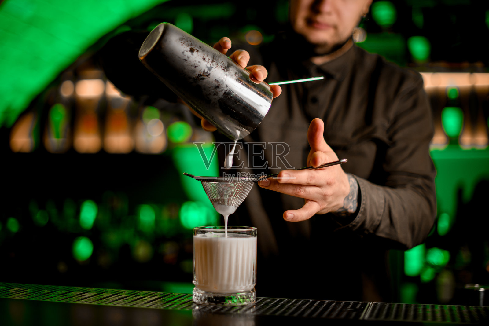 调酒师精确地将鸡尾酒从摇酒器通过筛子倒入加冰的老式玻璃杯中照片摄影图片