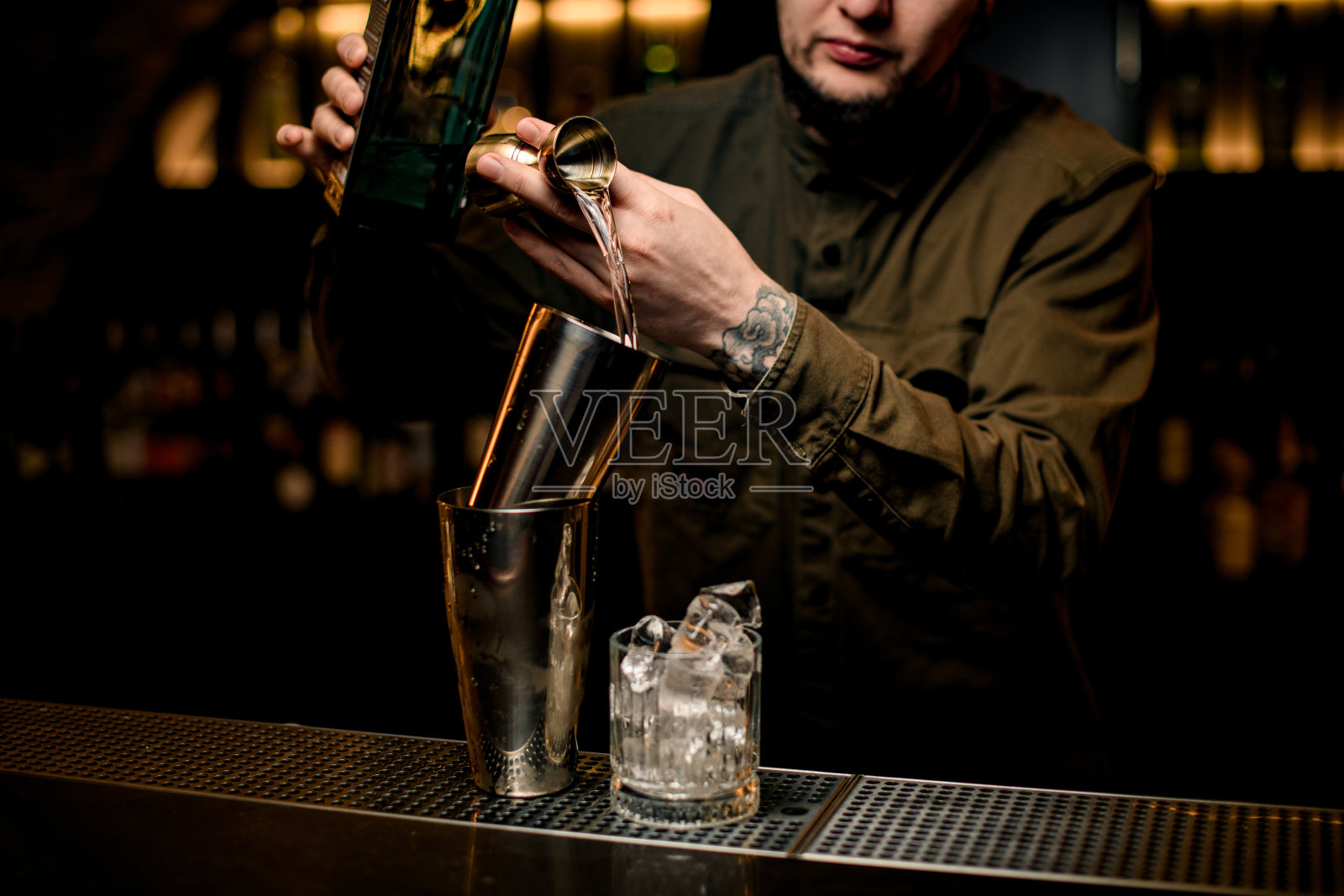 在酒吧，一名男子轻轻地将饮料从搅拌器倒入吧台的钢制摇杯中照片摄影图片