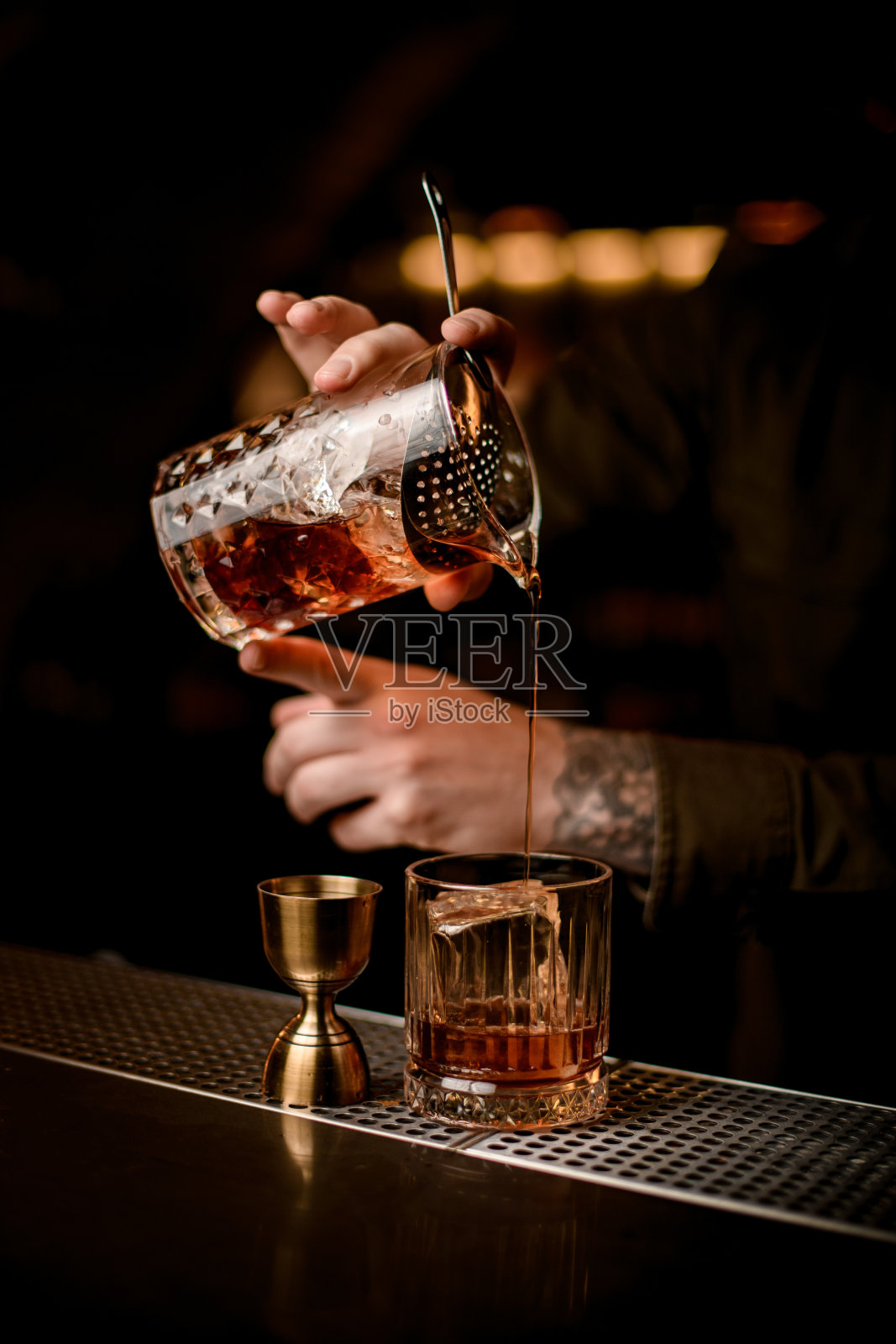 特写的调酒师的手握混合杯，并将鸡尾酒倒入玻璃杯照片摄影图片