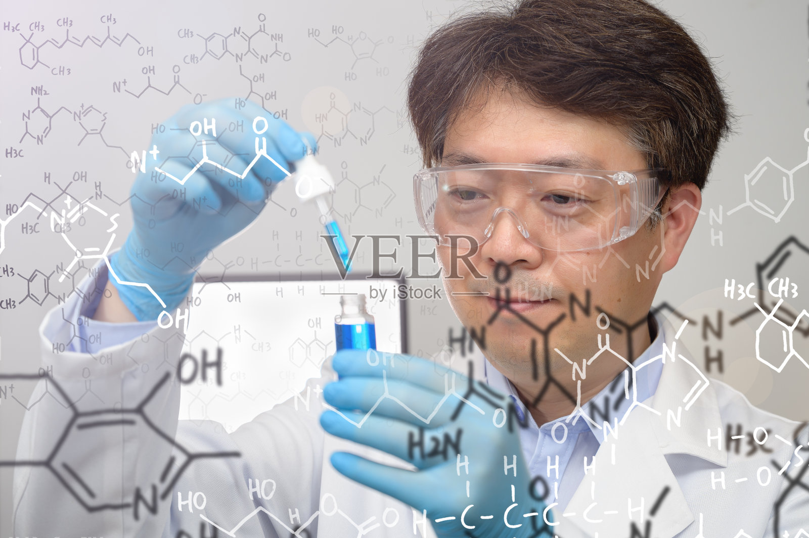 一位中年亚洲男性科学家的肖像穿着白色的实验室长袍和手套，手里拿着一个实验容器。照片摄影图片