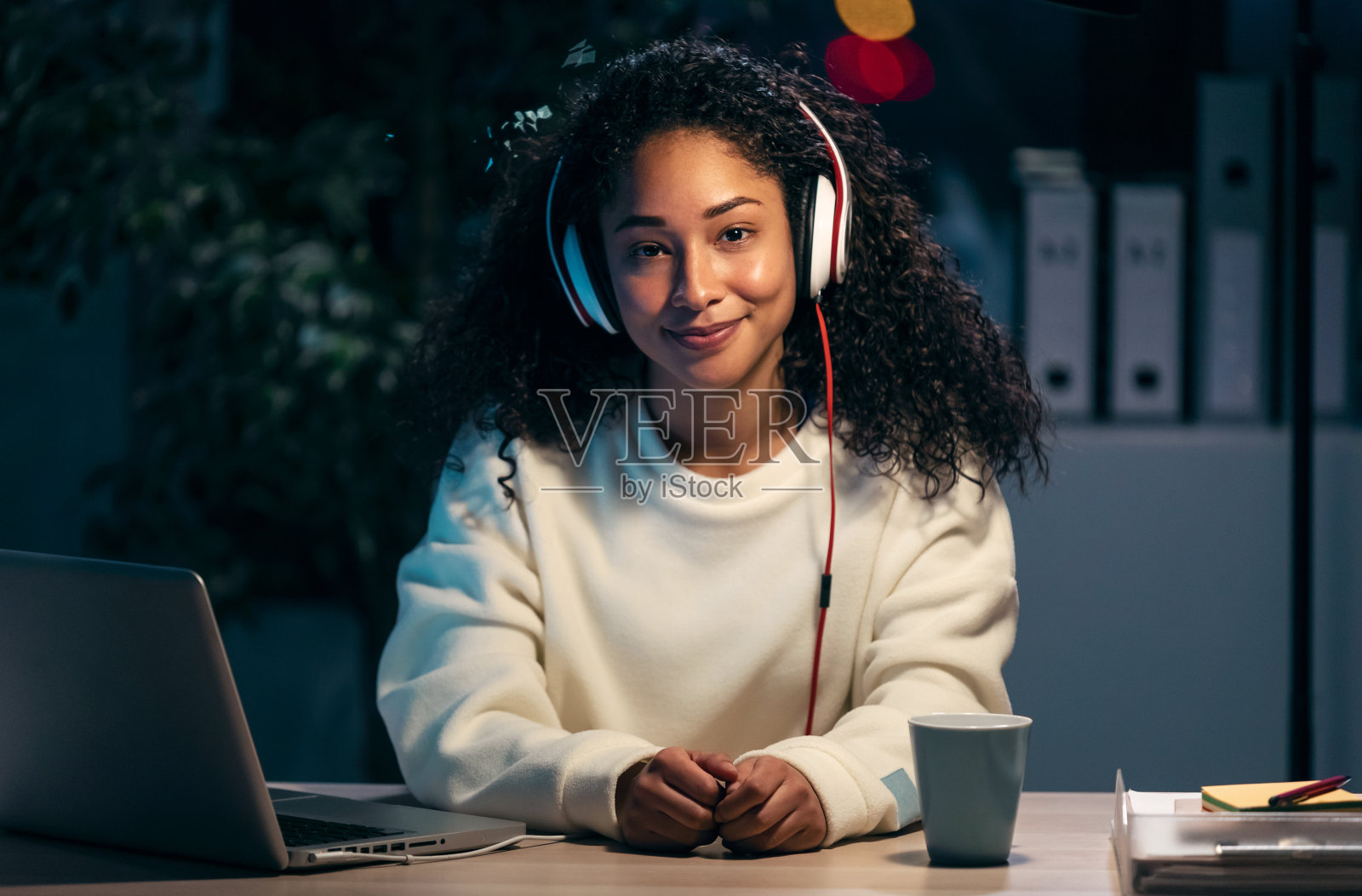 自信的非洲女性听音乐耳机，同时放松工作在办公室在家。照片摄影图片