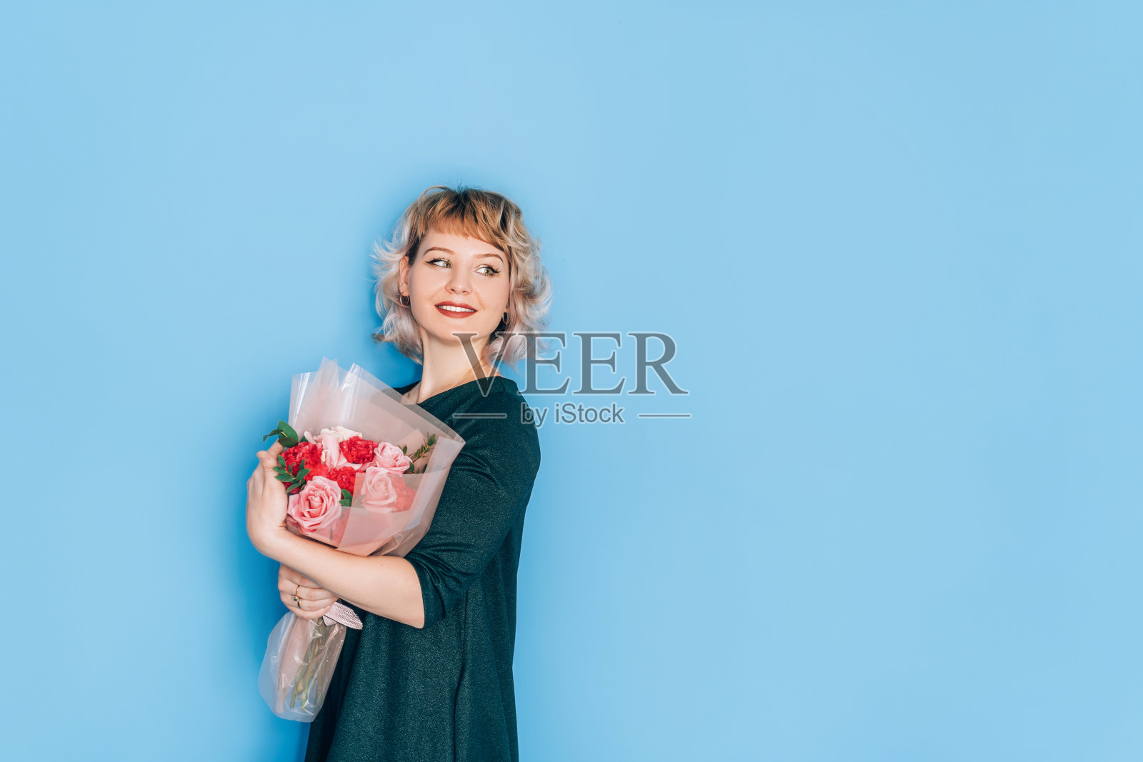 在蓝色背景前，穿着衣服的女人拿着一束美丽的鲜花。节日礼物情人节，2月14日，3月8日，母亲节照片摄影图片