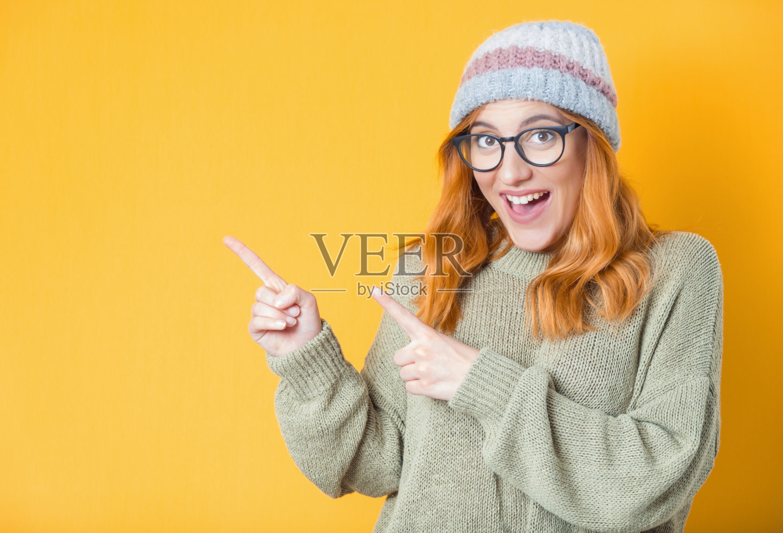 年轻女子惊讶地站着，指着空白的地方——抄写空间。女孩笑得很开心，半长身体，孤立在白色的背景上照片摄影图片