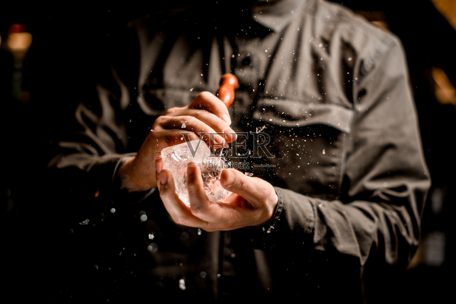 酒保拿着一块冰，熟练地用三叉戟把它压碎照片摄影图片