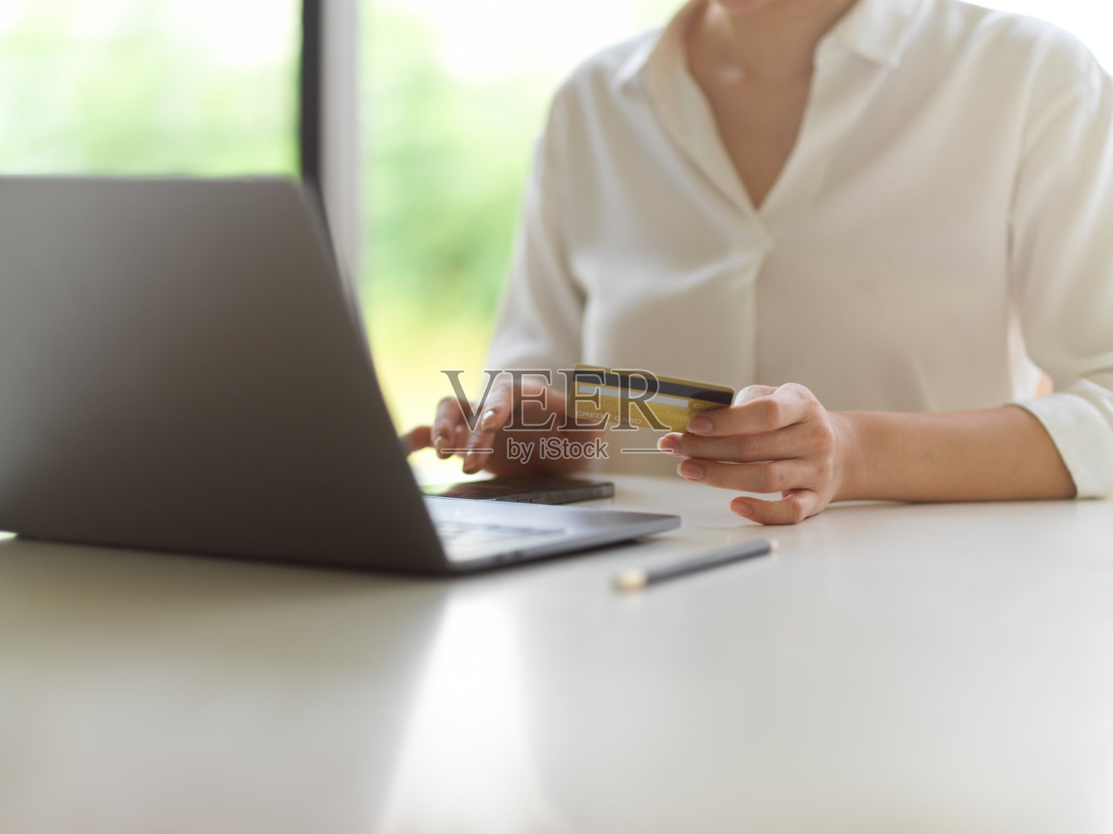 女性手握信用卡，触碰智能手机屏幕，白色桌上放着笔记本电脑照片摄影图片