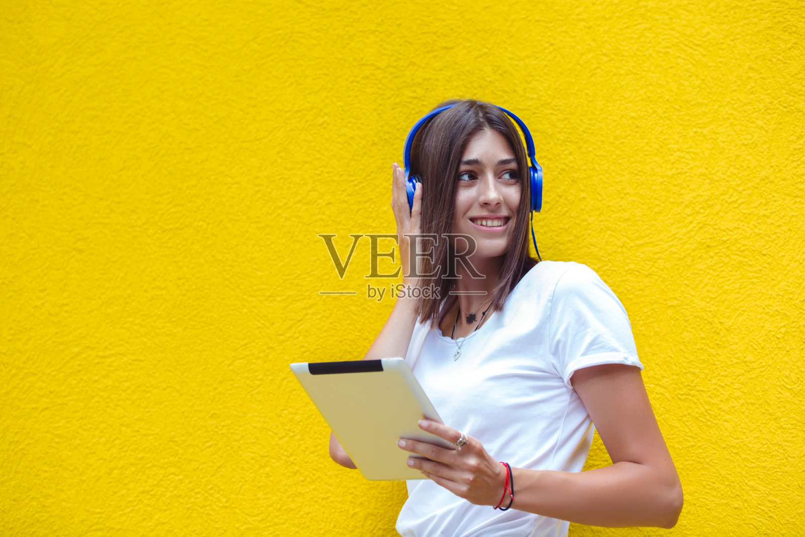 一名年轻女子坐在黄色的墙上，戴着耳机在平板电脑上听音乐照片摄影图片