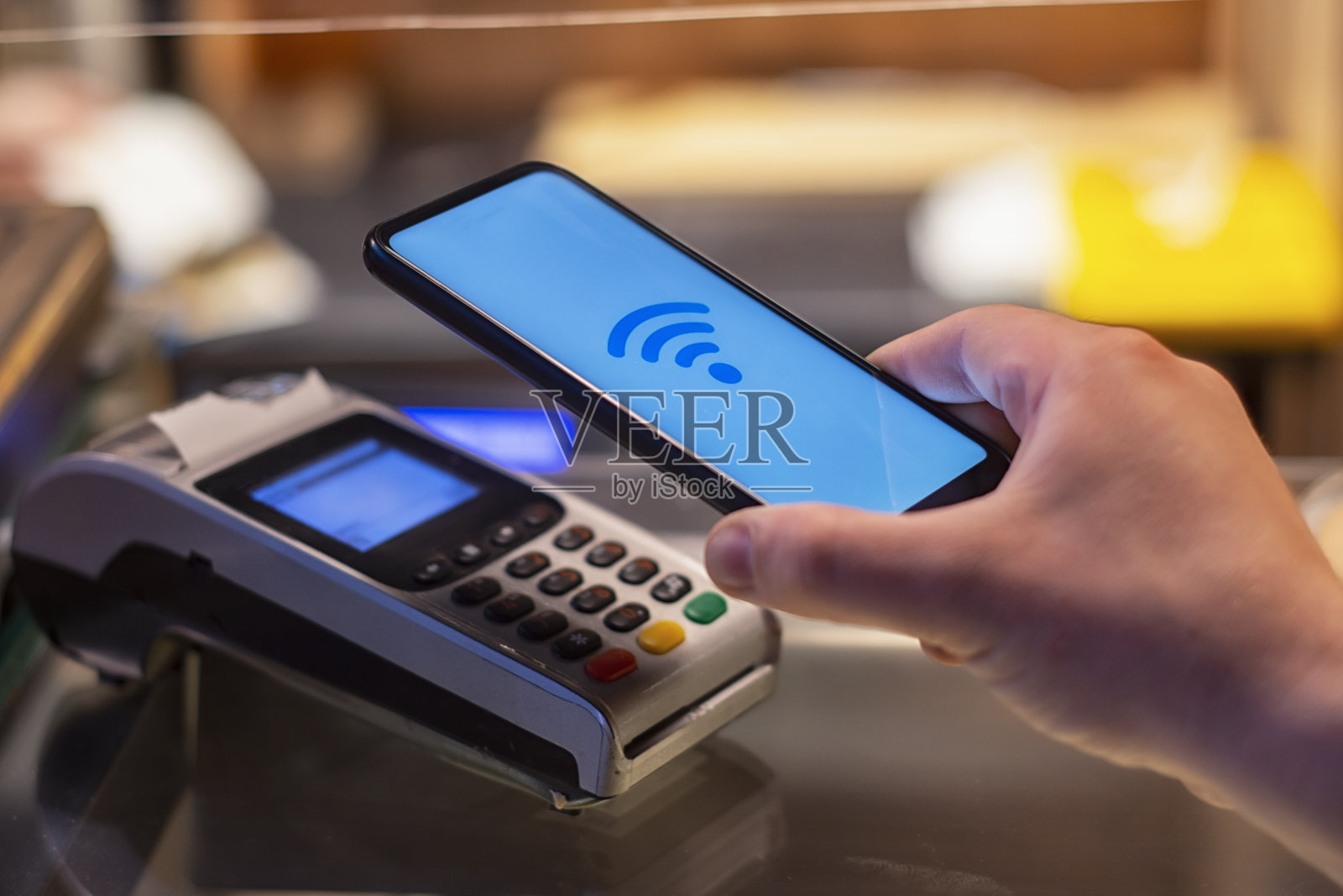 顾客在商店用智能手机支付，使用NFC技术。以支付终端为背景。照片摄影图片