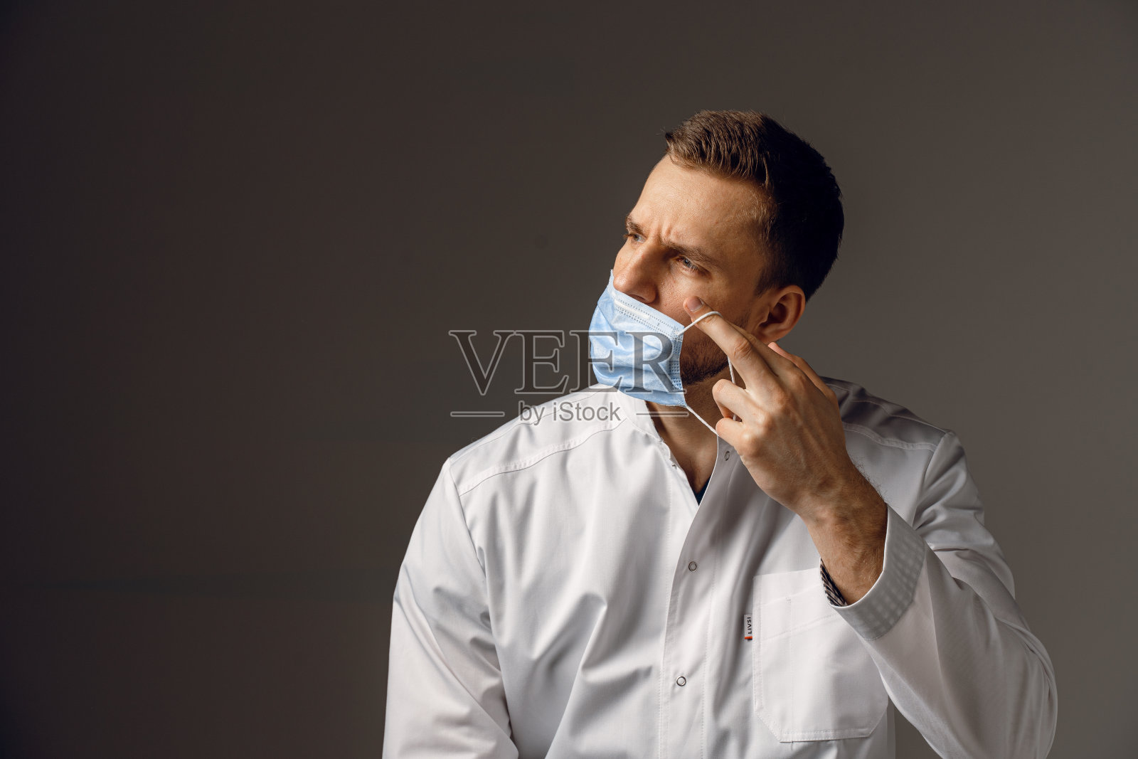 医生戴医用口罩，预防covid-19。第三波冠状病毒疫情时保护健康的建议。英俊的男人穿着医袍照片摄影图片