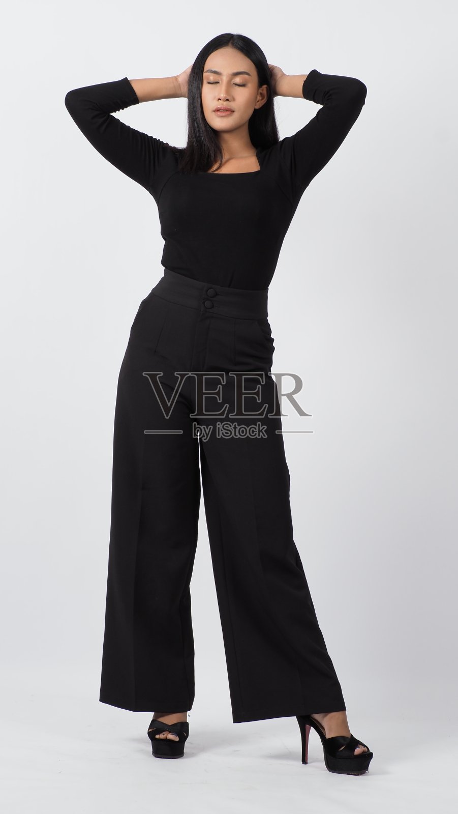 一名年轻女子穿着黑色衬衫和裤子在工作室里摆姿势，背景是白色。性感的亚洲黑发女孩与丰满的嘴唇pose相机。有吸引力的女性与大乳房。在摄影棚拍摄。照片摄影图片