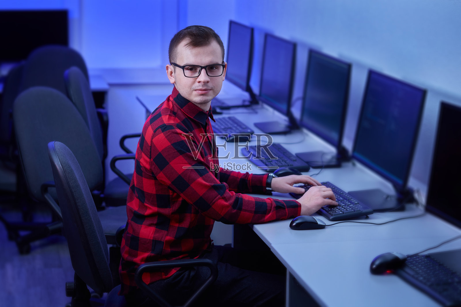 一个穿红衬衫戴眼镜的年轻人。在办公室工作。照片摄影图片