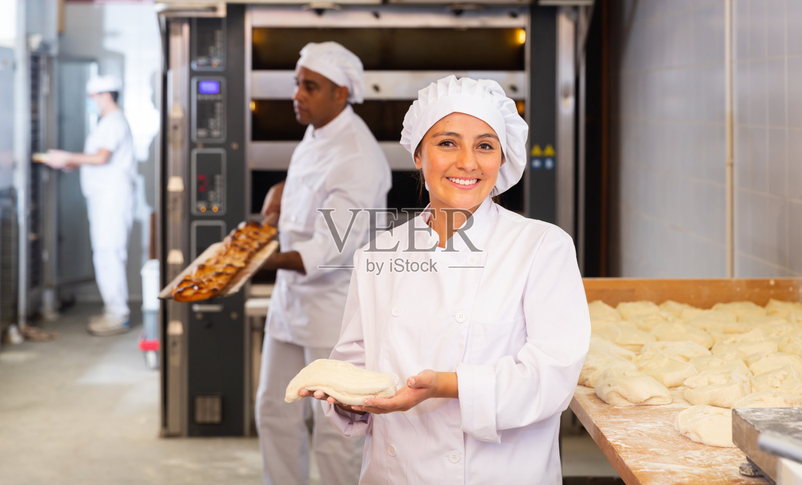 微笑的女面包师拿着生面团在面包房照片摄影图片