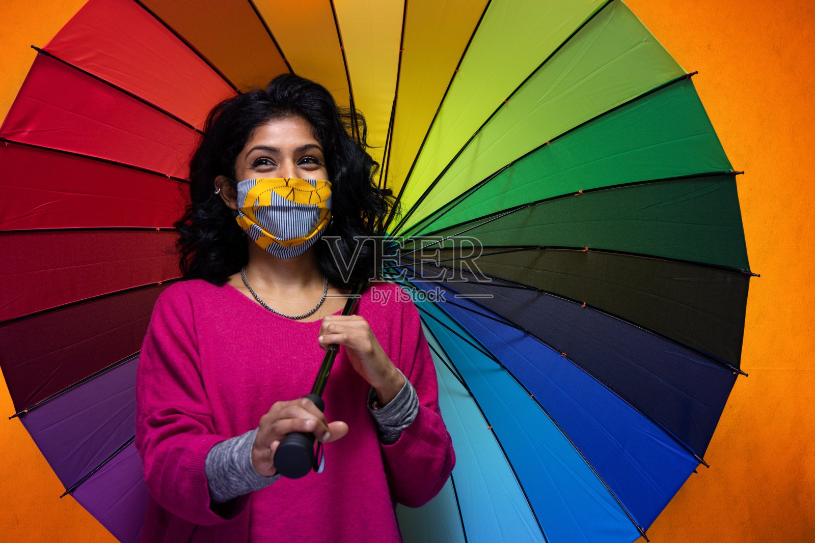 美丽的年轻印度妇女与彩色伞与covid - 19口罩保护-美丽的斯里兰卡女孩使用保护从大流感，同时用一个全彩色大伞覆盖自己照片摄影图片