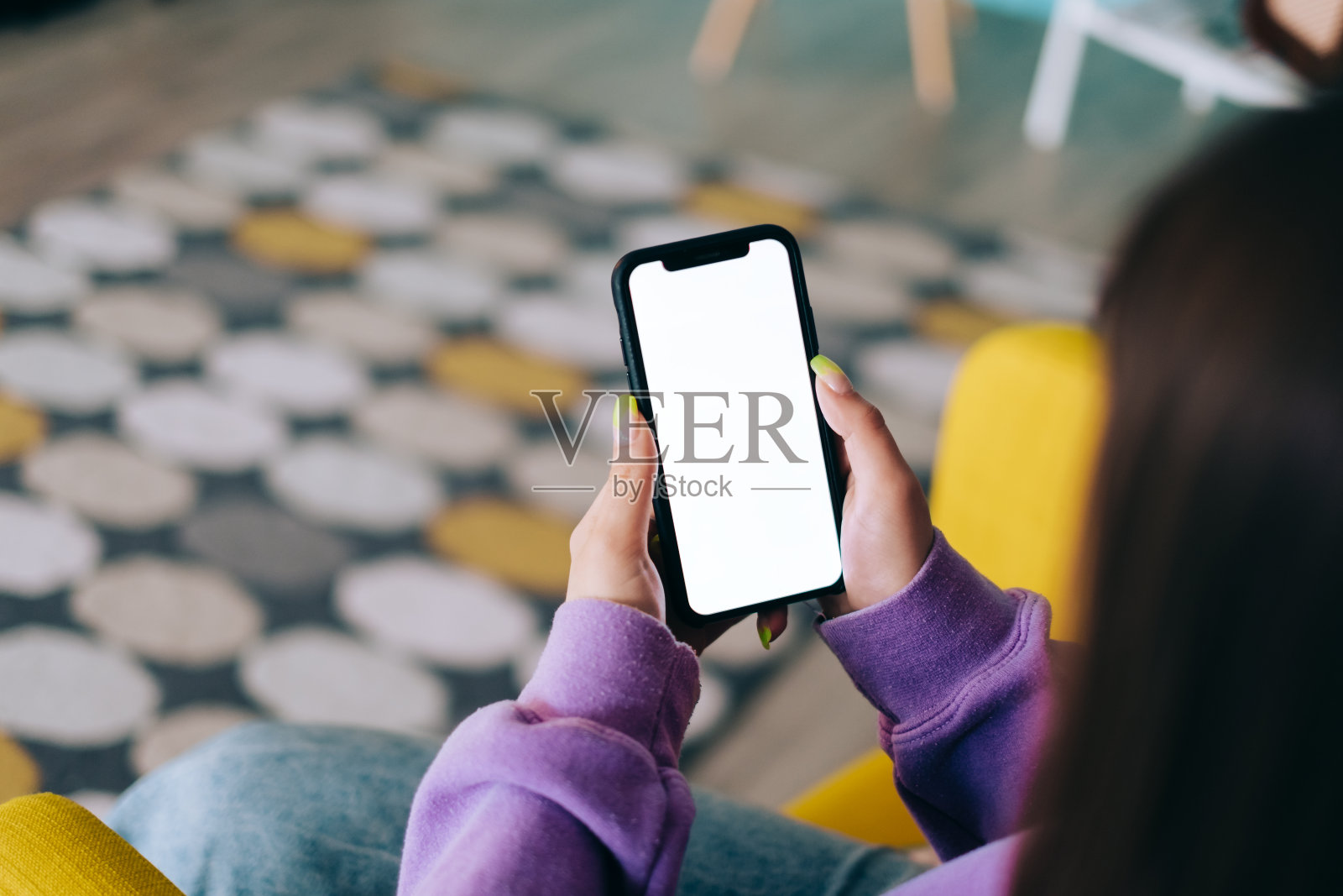 一个女人正坐在家里客厅的扶手椅上，手里拿着一部白色屏幕的智能手机。照片摄影图片