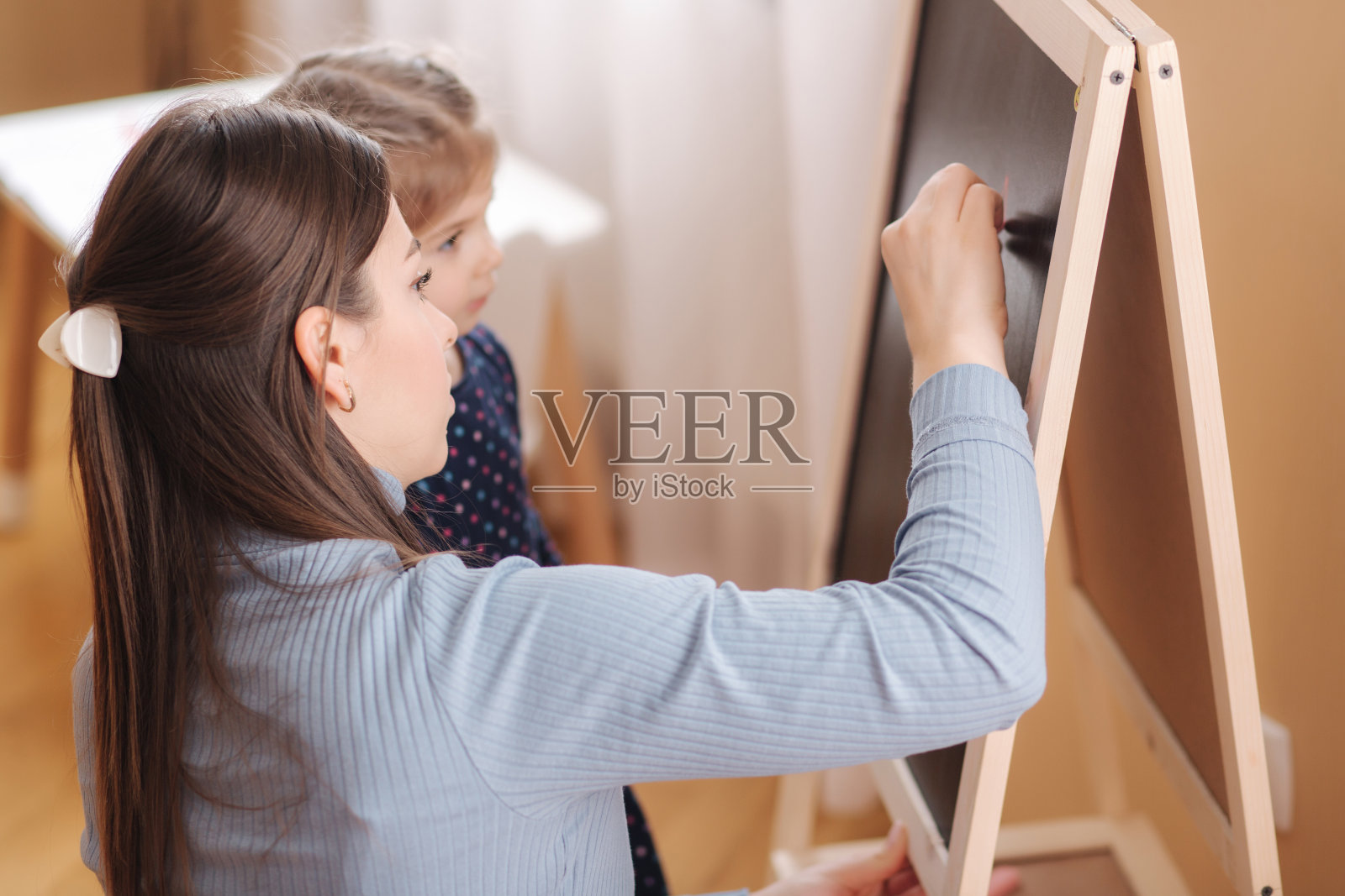 可爱的小女儿带着年轻的妈妈在家里的黑板上学习写字母。女性儿童在服装学习方面的侧视图照片摄影图片