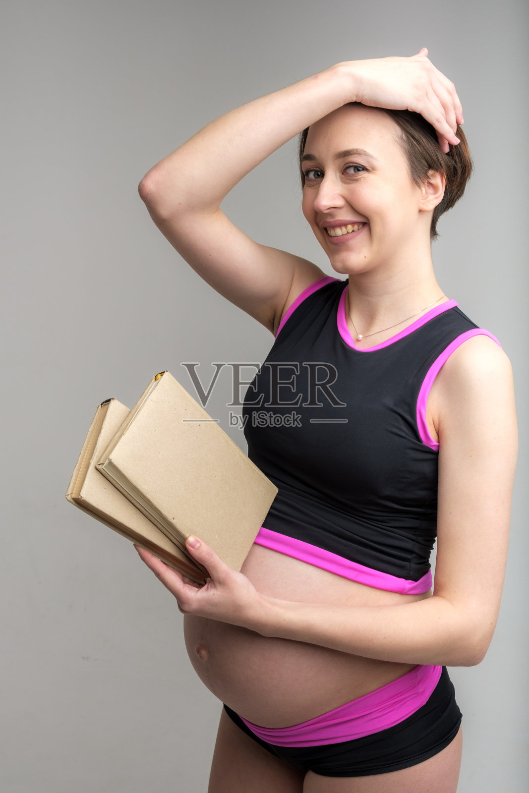 工作室肖像年轻的成年孕妇抱着一堆书，准备婴儿出生的概念，白色的背景照片摄影图片