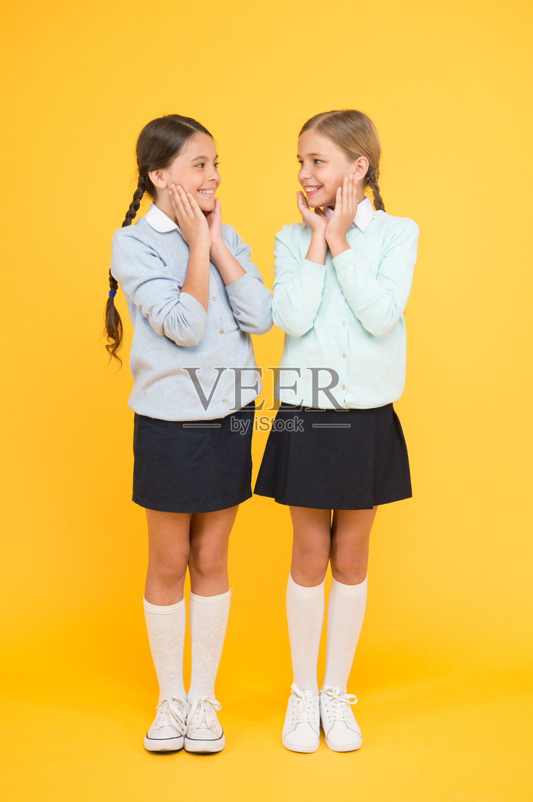 看看这个。孩子的时尚。友谊和姐妹。教育的概念。回到学校。穿校服的快乐女孩。聪明的小女孩在黄色背景。知识的一天。童年的快乐照片摄影图片