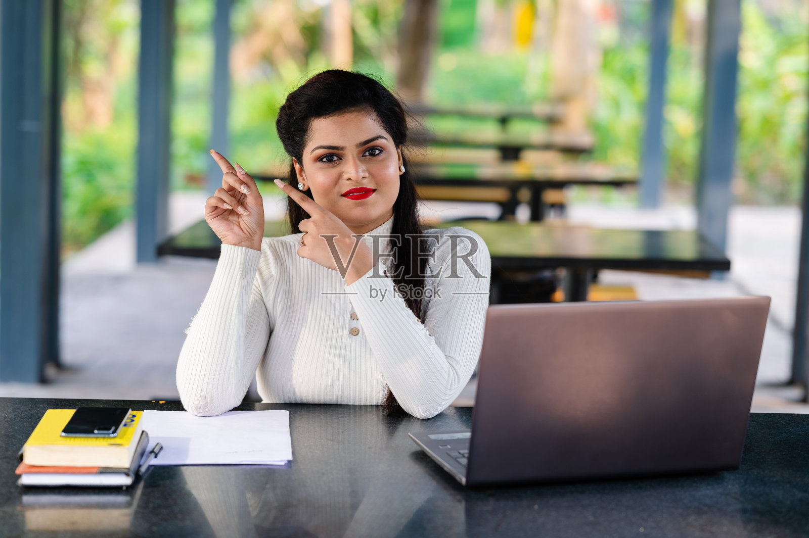 年轻女子一边用笔记本电脑一边指着旁边的东西照片摄影图片