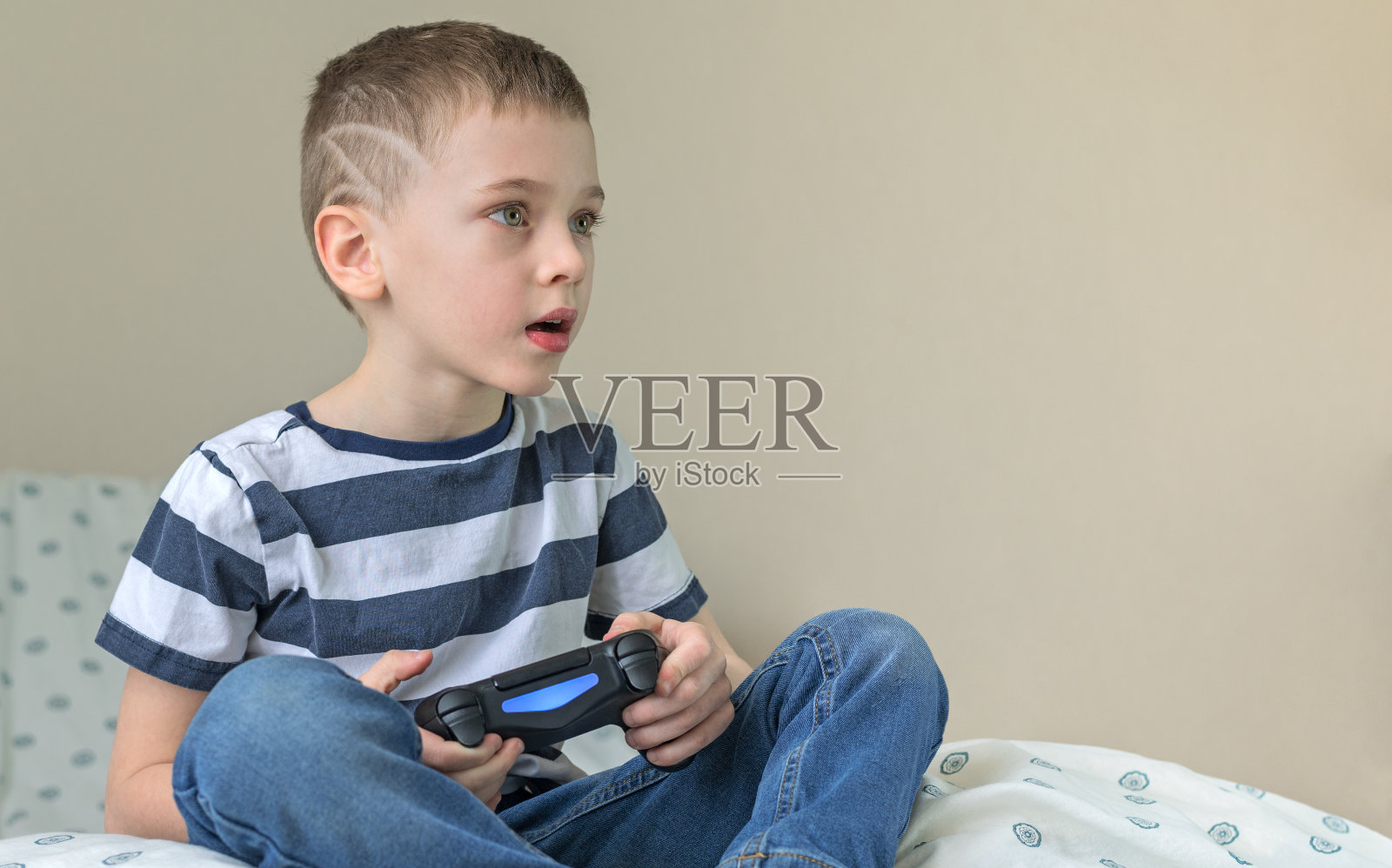 热情的小男孩拿着手柄在家玩电子游戏。照片摄影图片