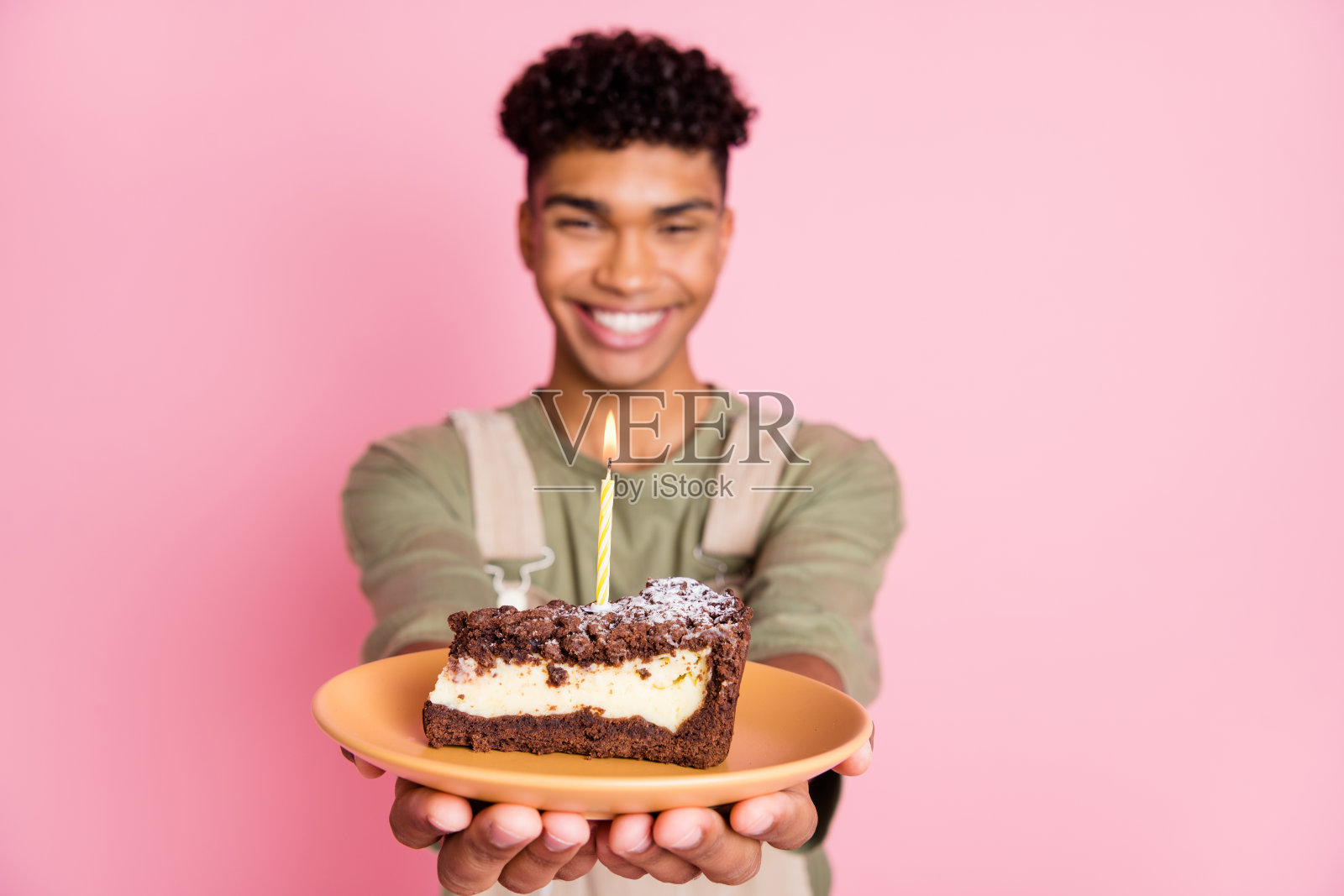 卷发男孩的照片肖像保持盘子与蜡烛在生日蛋糕微笑孤立在柔和的粉红色背景照片摄影图片