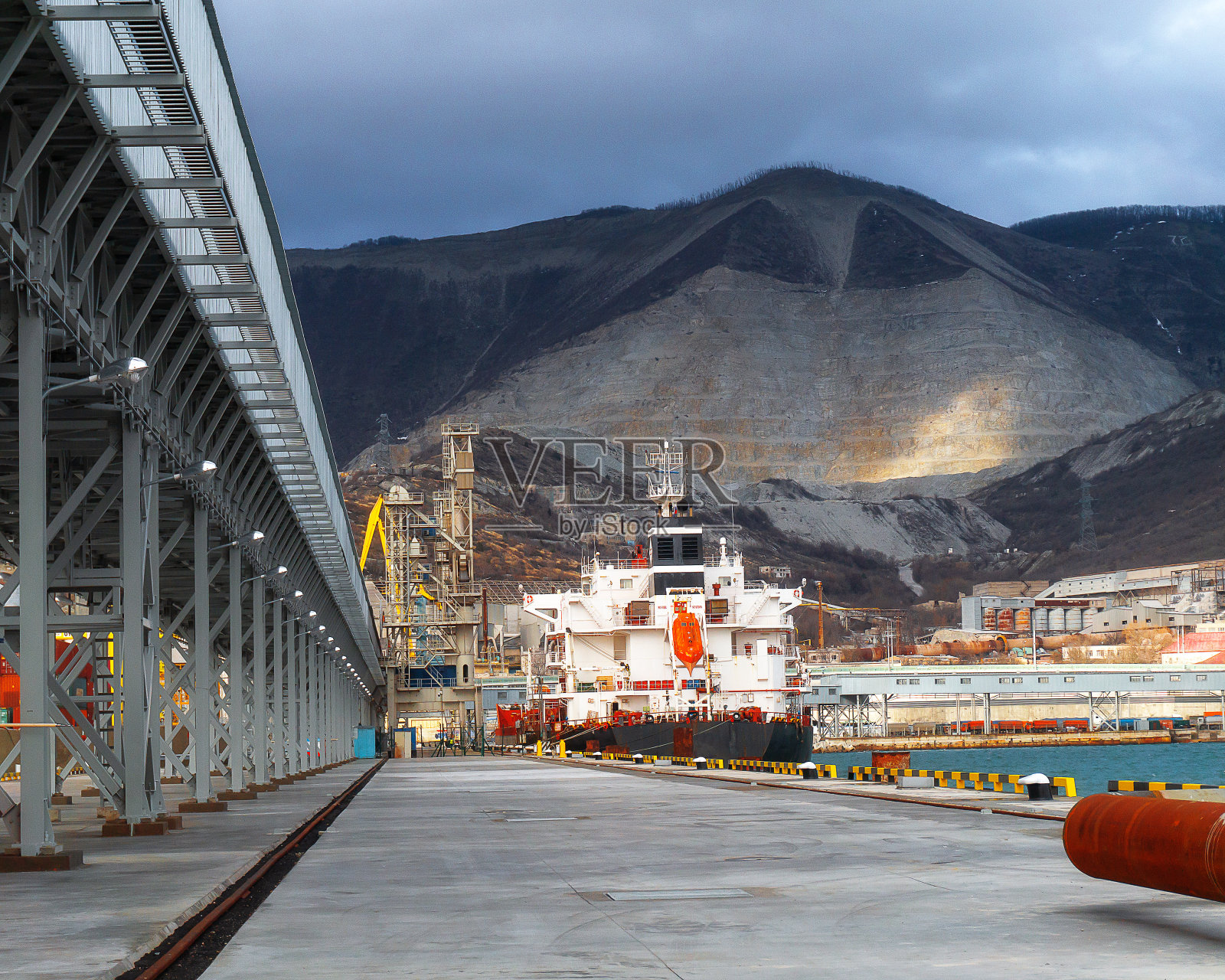 一艘干货船站在港口的码头上，背靠群山照片摄影图片