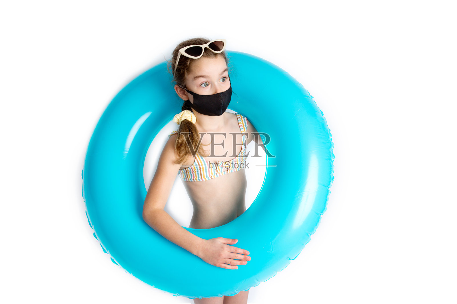 可爱的小女孩身穿沙滩泳衣，围着绿松石充气圈，戴着黑色covid-19防护面具。冠状病毒感染期间的娱乐概念。照片摄影图片