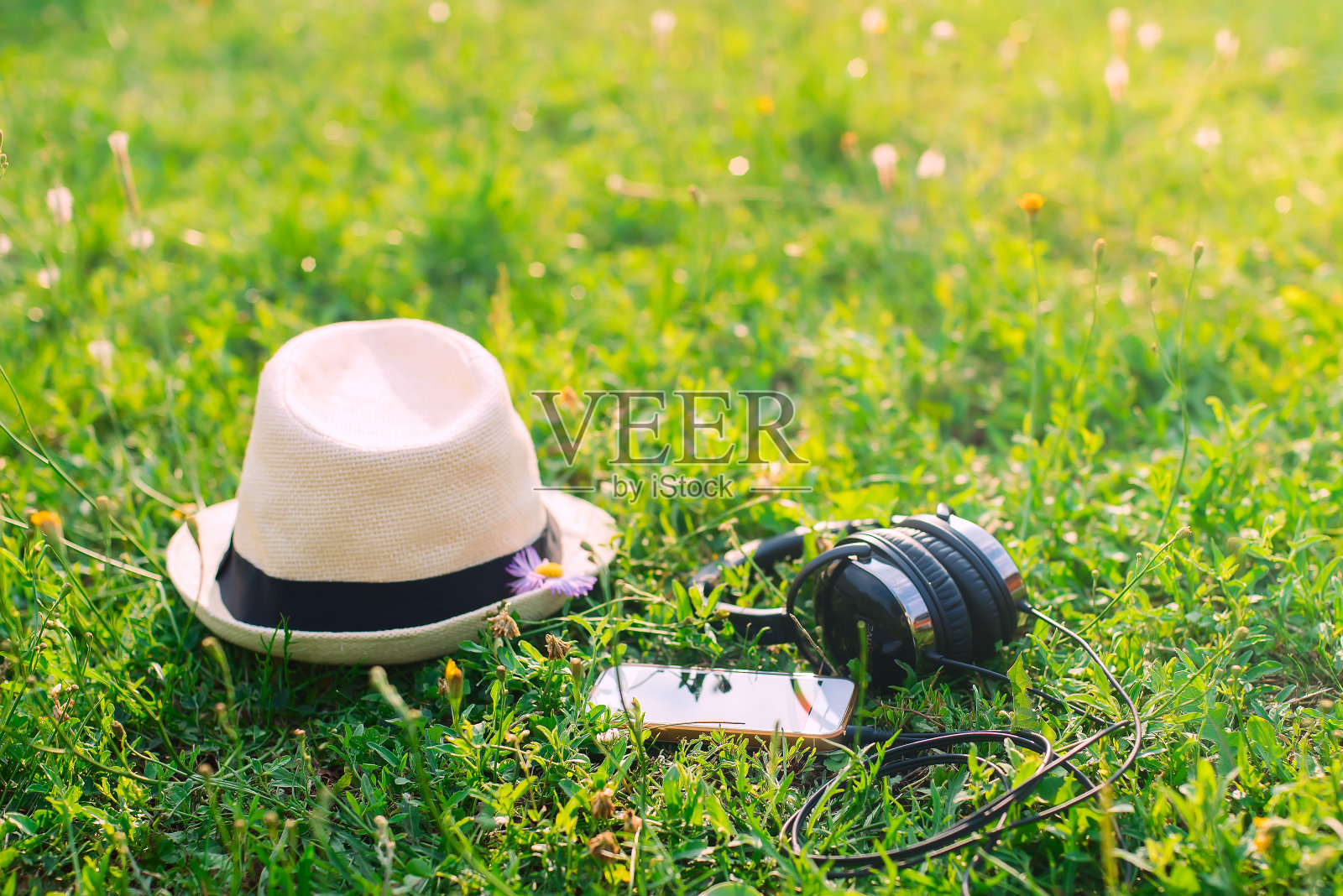 待在公园里。日落时分，在绿油油的草地上戴上帽子、耳机和手机。照片摄影图片