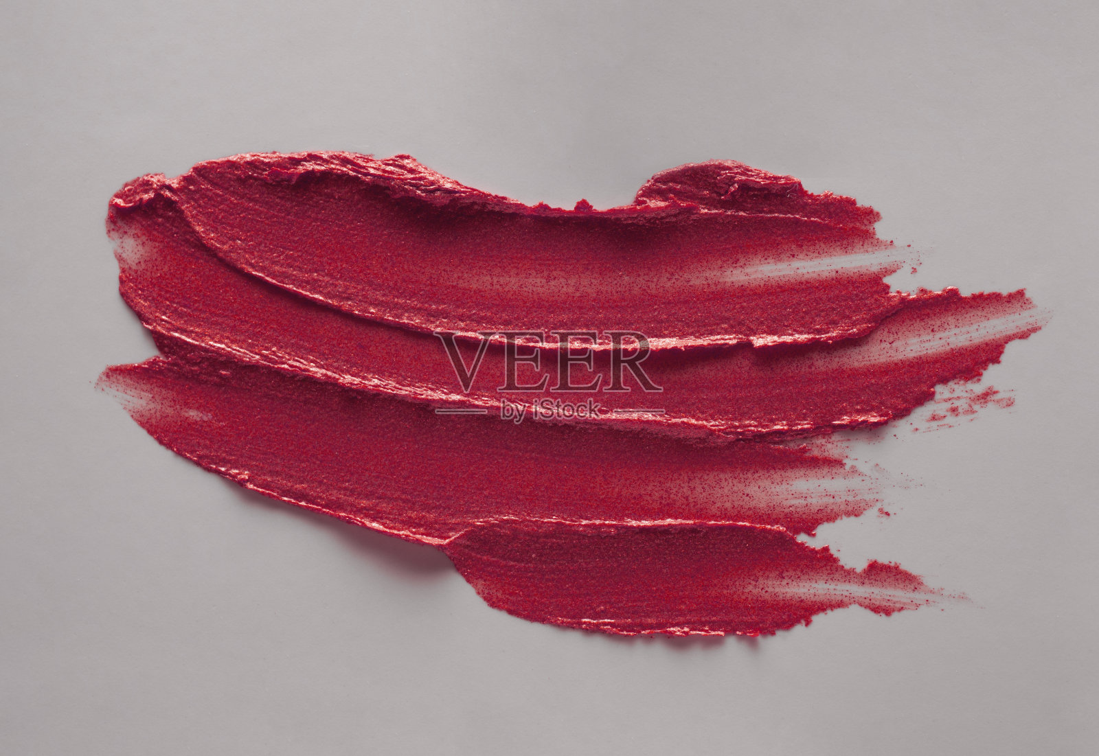 在灰色孤立的背景上涂抹了充满活力的红色深粉红色，深栗色纹理的口红照片摄影图片