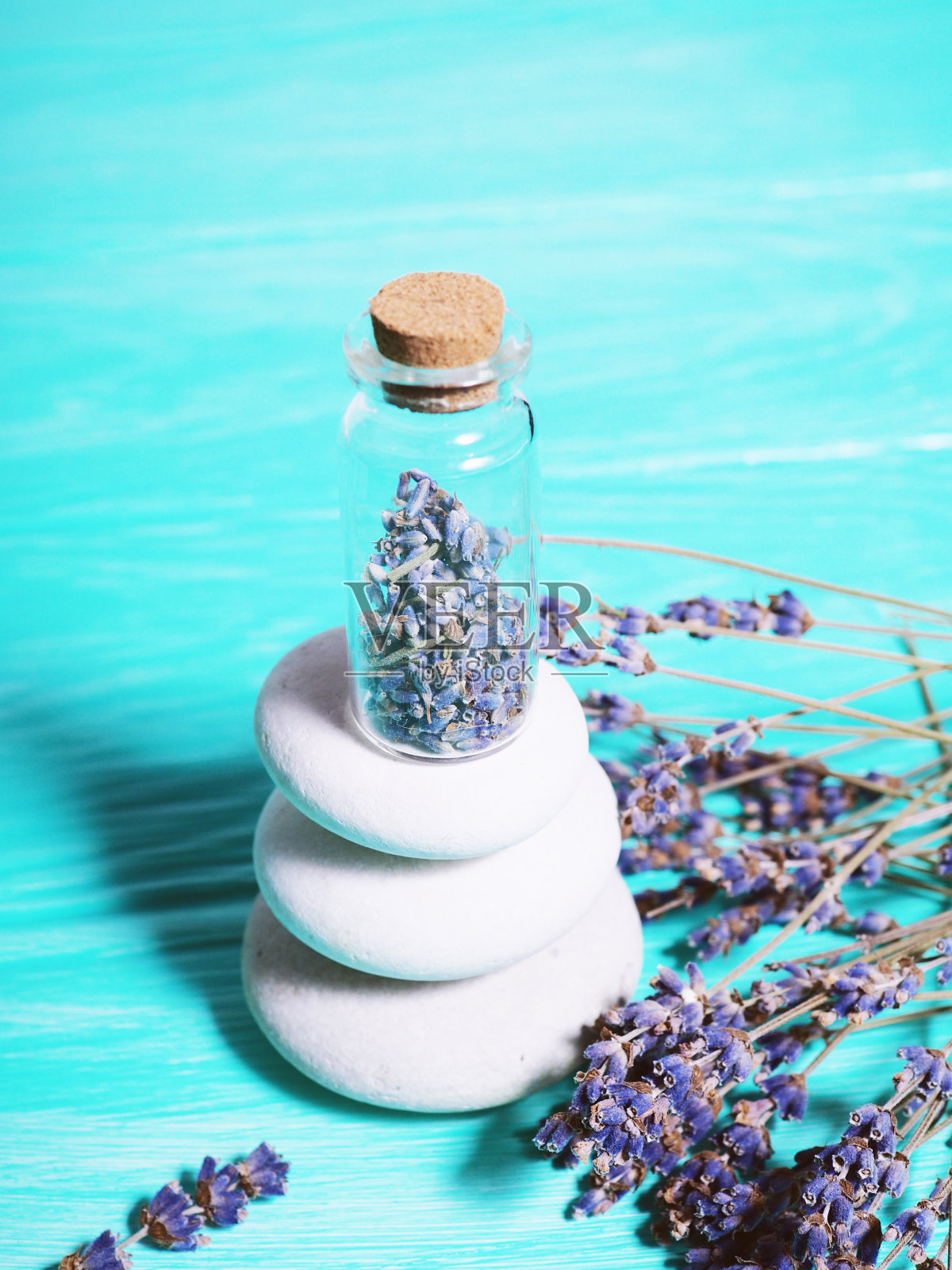 禅宗的石头堆在蓝色的木质背景上，薰衣草种子在瓶子里，薰衣草树枝在旁边照片摄影图片