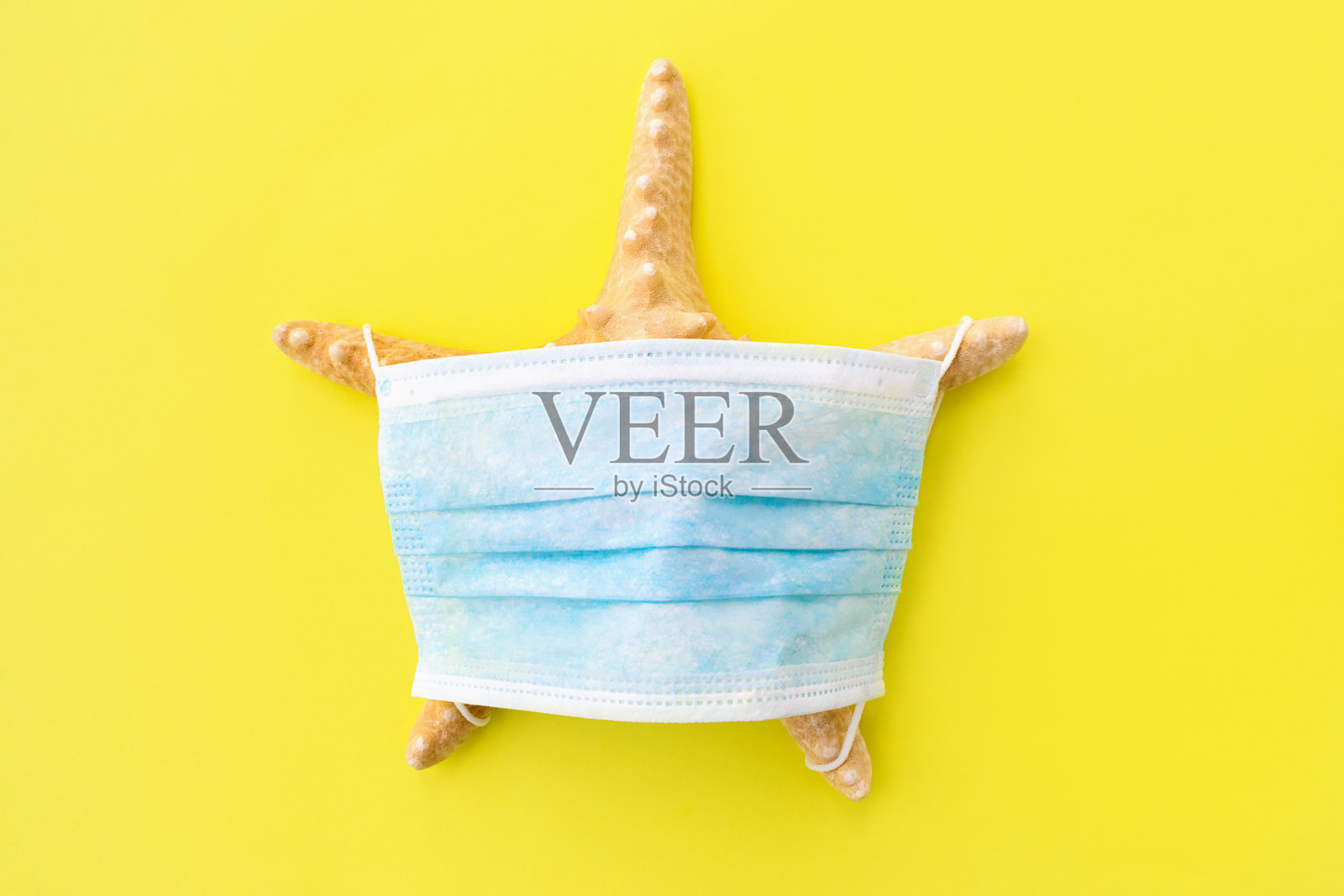 黄色背景上的海星和防护面罩。因新冠肺炎大流行取消暑假和旅游的概念。夏天的概念。选择聚焦,俯视图照片摄影图片