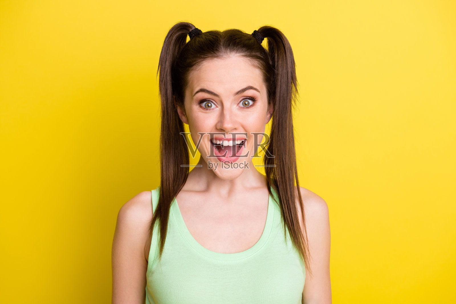 照片的可爱印象深刻的年轻女孩穿绿色坦克顶张着嘴孤立黄色背景照片摄影图片