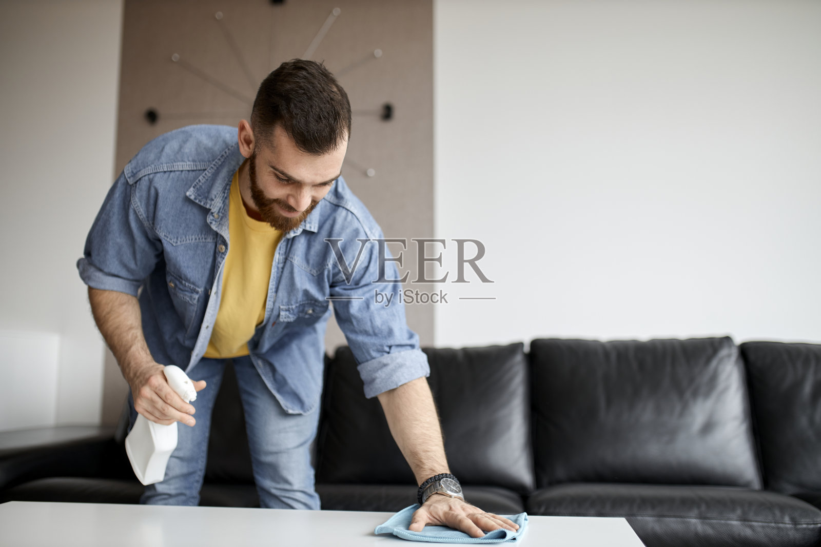 在他的公寓里，一个男人正在用抹布和喷雾器清理餐厅的桌子。一个英俊的年轻人正在打扫他的家。家务不仅仅是女人的专利。照片摄影图片