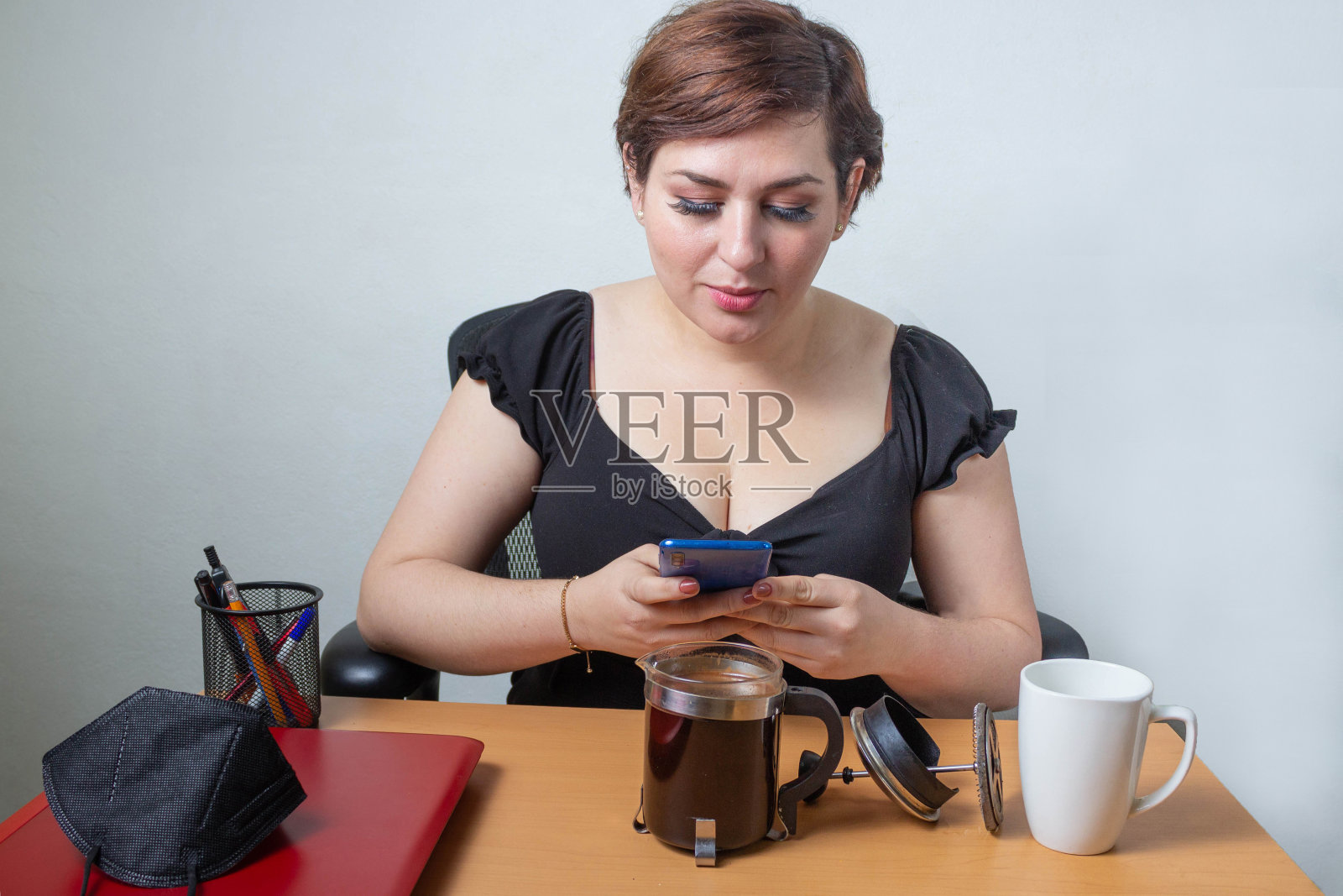 一个在办公室用手机准备法式咖啡的女人照片摄影图片