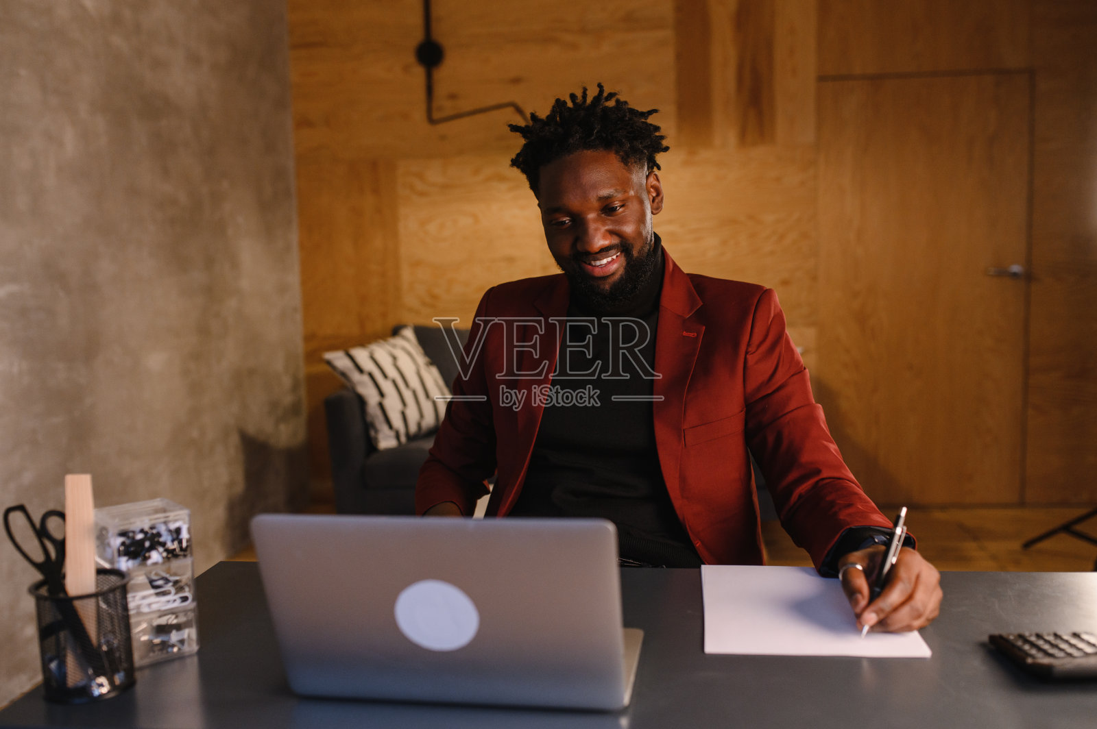 专注于非洲年轻商人戴耳机在线学习，在笔记本电脑上观看网络播客，听学习教育课程，会议，电话，做笔记坐在办公桌前，电子学习的概念照片摄影图片