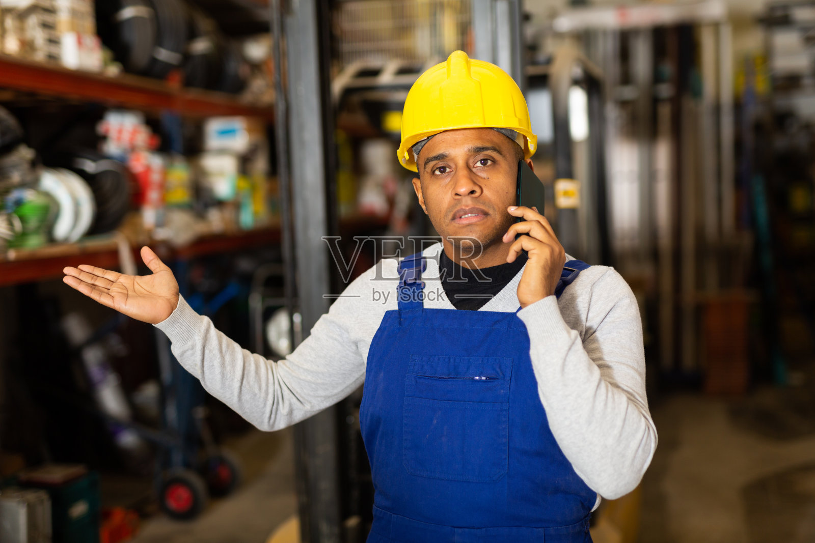 拉丁美洲人，穿着蓝色工装裤，在建筑大卖场里打电话照片摄影图片