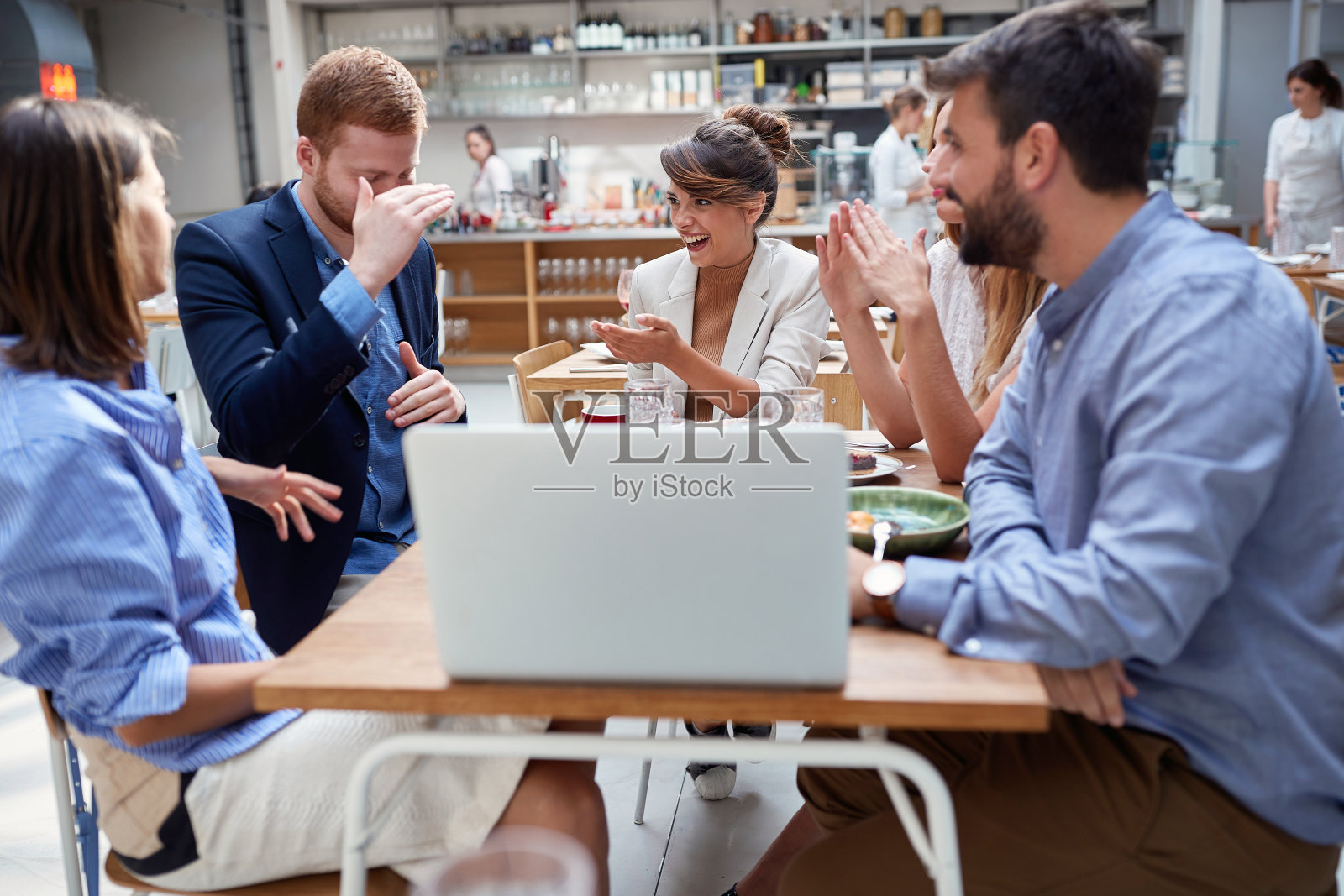 一群有创造力的人坐在桌旁，用笔记本电脑工作，在咖啡馆讨论。照片摄影图片