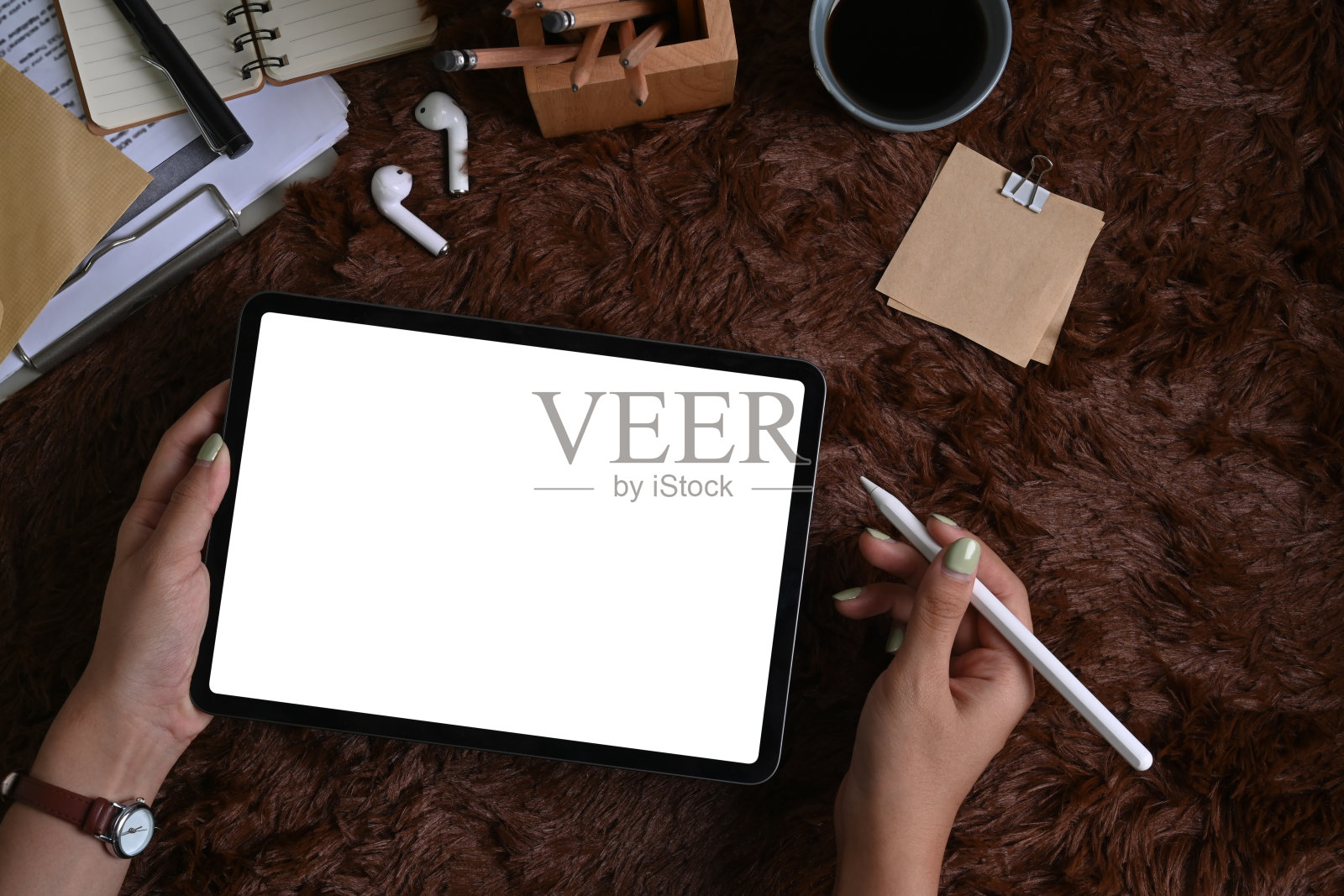 头顶拍摄的女性拿着数字平板电脑在棕色毛茸茸的毛皮地毯上。照片摄影图片