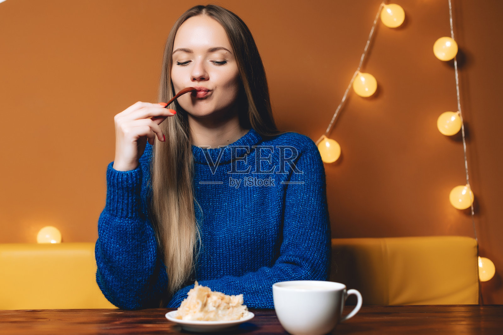 年轻女子正在室内喝咖啡。女人像一杯热饮。女孩吃着甜蛋糕，享受着照片摄影图片