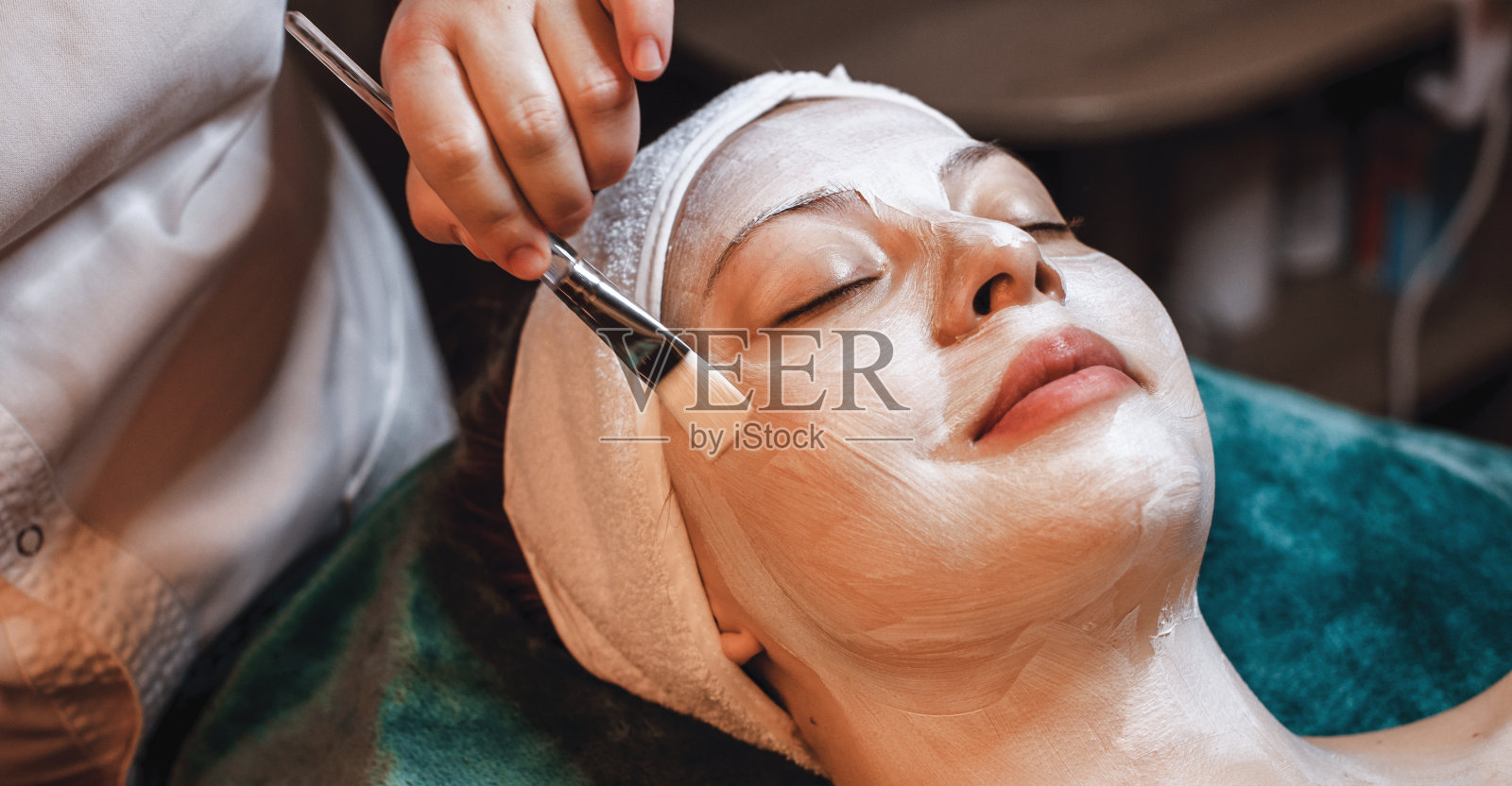 白种人女士有一个皮肤护理程序在面部与涂抹霜刷在水疗中心照片摄影图片