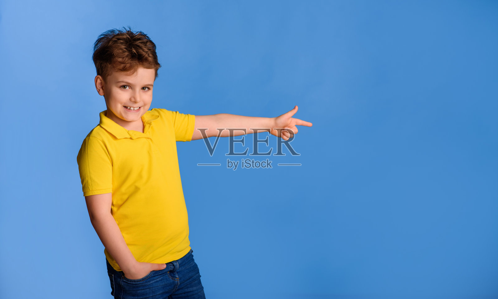 穿着黄色t恤的快乐小男孩指着蓝色的背景笑着。照片摄影图片