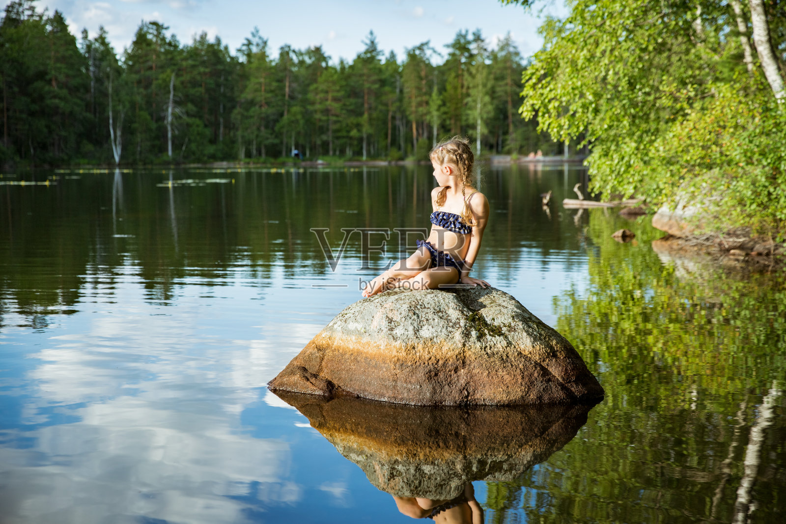可爱的小女孩坐在湖里的一块岩石上照片摄影图片