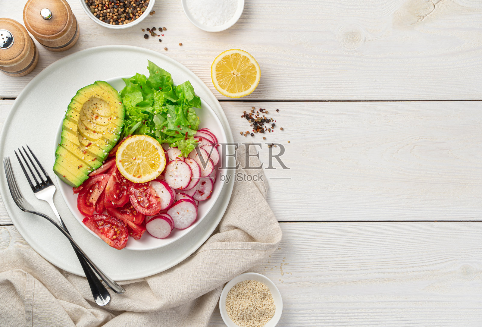 白木背景上的新鲜蔬菜沙拉。牛油果、萝卜、番茄、生菜片，加芝麻及香料调味照片摄影图片