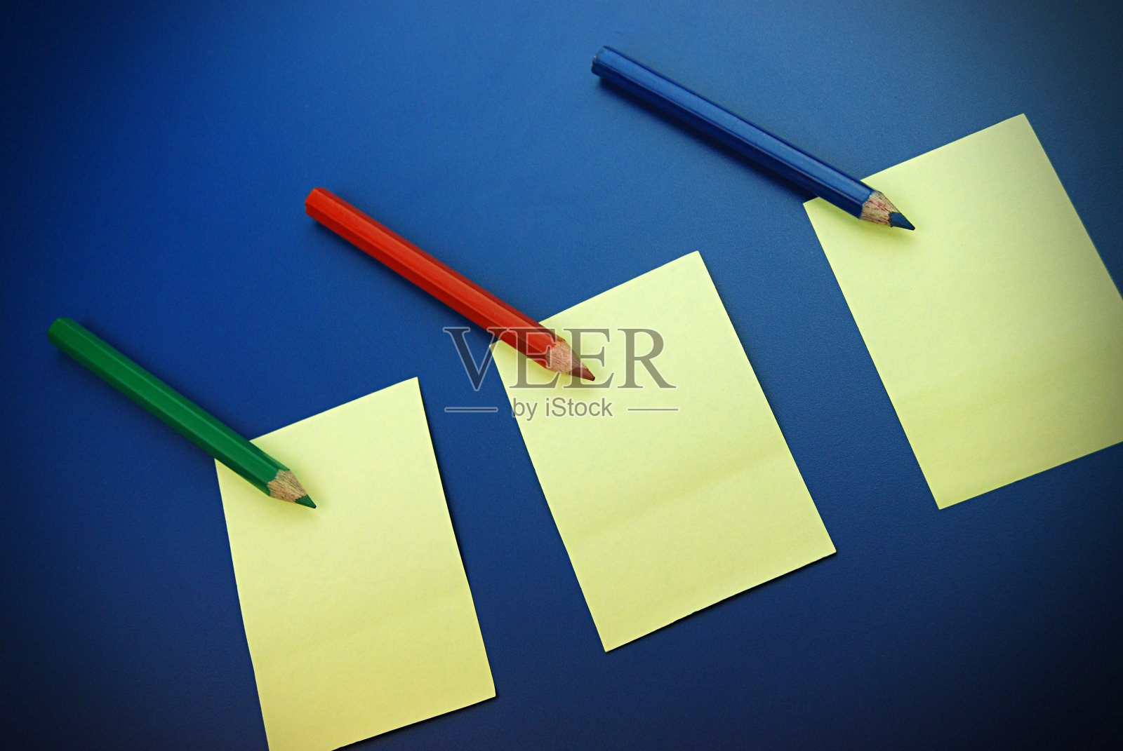 三种原色铅笔(RGB或红、绿、蓝)的俯视图排列在黄色便利贴上，贴在深蓝色背景上照片摄影图片