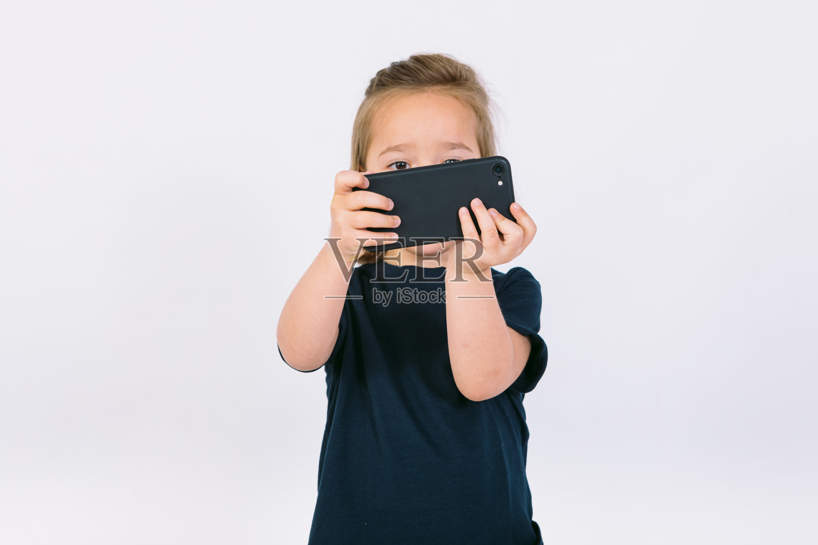 金发小女孩手里拿着手机，在玩游戏照片摄影图片