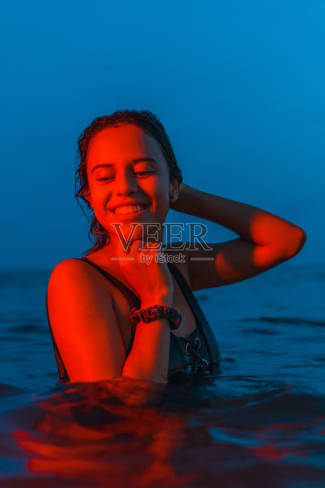 一个年轻漂亮的白人褐发女人的生活方式晚上在海边沐浴着红光，蓝色的时刻照片摄影图片