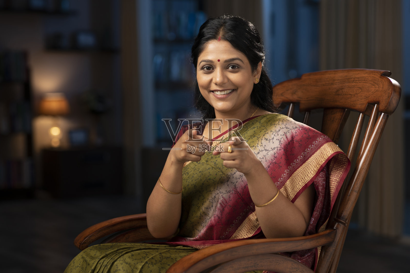 一个穿着纱丽的女人坐在家里的摇椅上，手指指着相机照片摄影图片