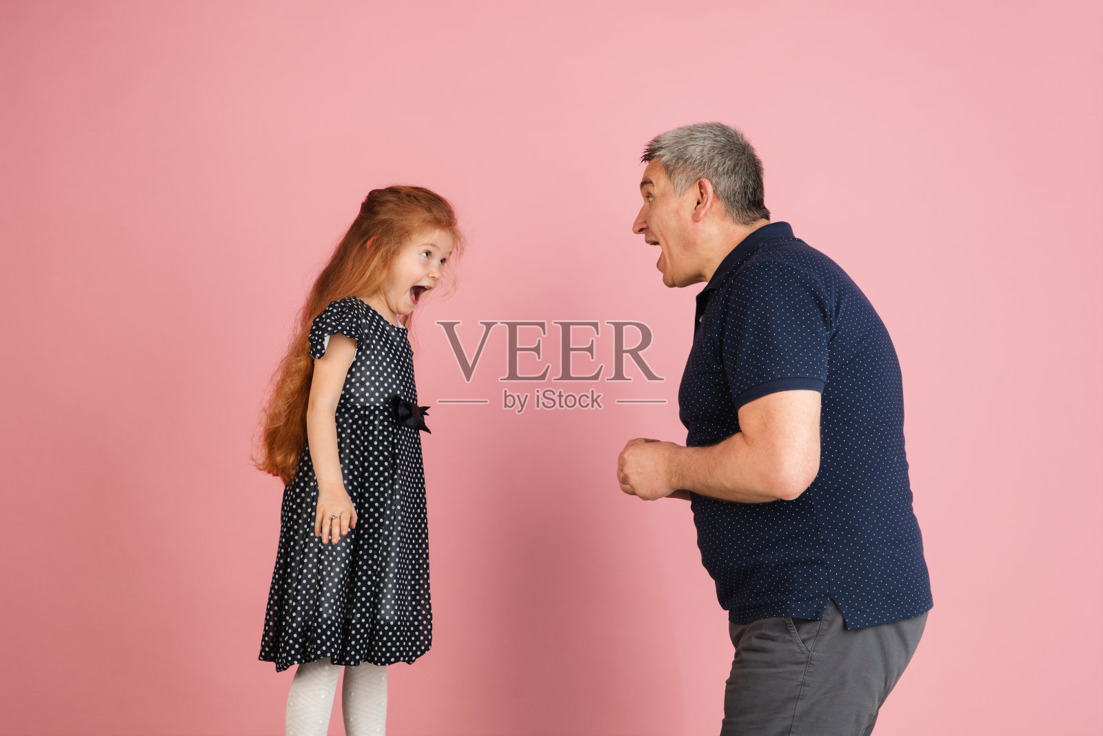 两个人，男人和小女孩，爸爸和女儿孤立在粉红色的背景下。照片摄影图片