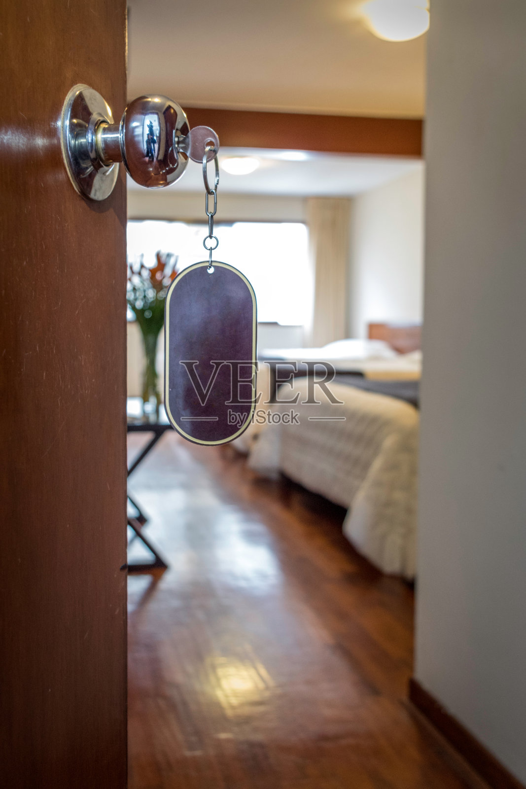 酒店的门上有一个钥匙圈来完成一个标志或一个品牌。在背景中你可以看到一些床，一个花瓶和一扇大窗户照片摄影图片