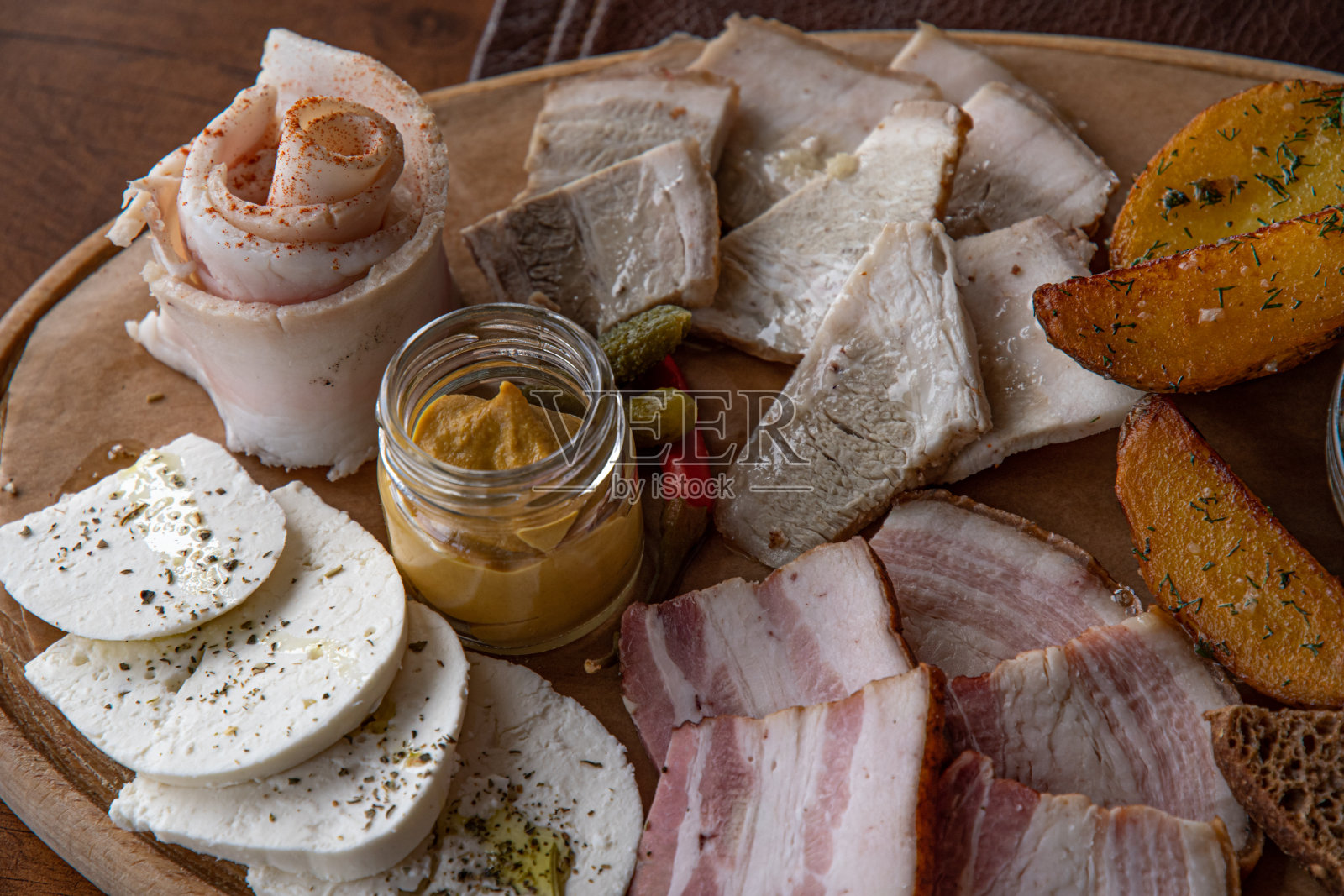 一盘质朴的木盘，里面装着各种各样的肉和奶酪开胃菜，还有烤土豆片和芥末照片摄影图片