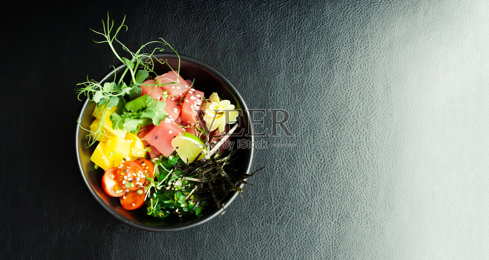 用碗盛金枪鱼沙拉。食材新鲜金枪鱼，圣女果，紫菜，米饭，大肚，柚子酱，照烧酱，海苔，芝麻，青柠，香菜。亚洲海鲜沙拉概念。照片摄影图片